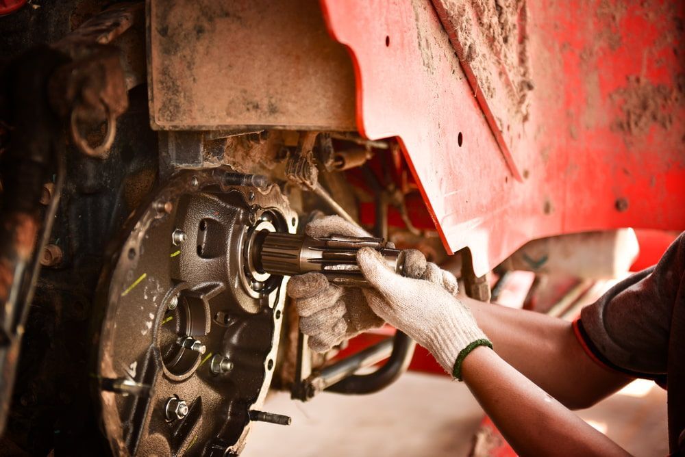 A Man is Working on a Red Tractor in a Garage — Nabiac Mower & Tractor Repairs in Forster, NSW