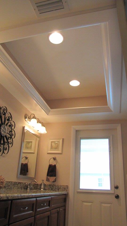 Bathroom with a recessed ceiling, lights, sink, mirror, door, and decorative wall pieces.