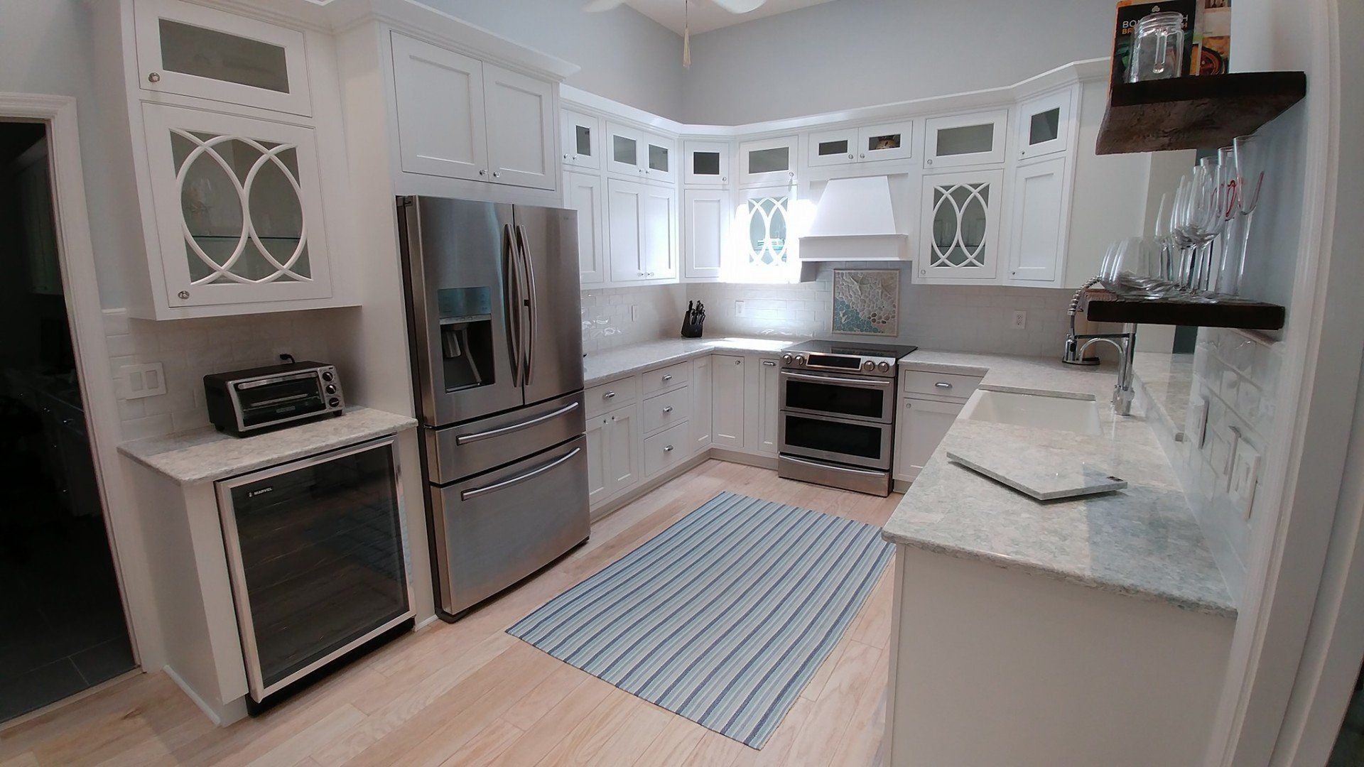 White kitchen with stainless steel appliances, light wood floors, and a blue striped rug.