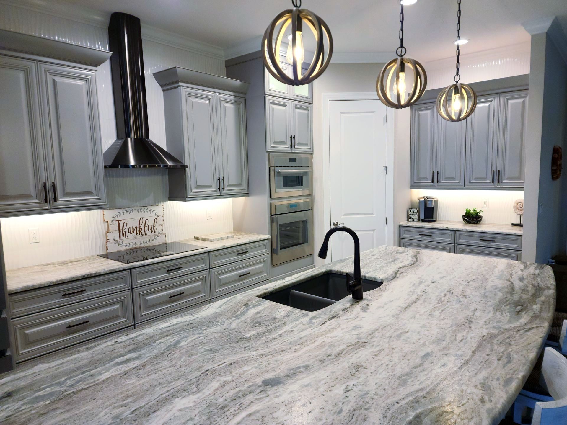 Gray and white kitchen with island, stainless steel appliances, and pendant lights.