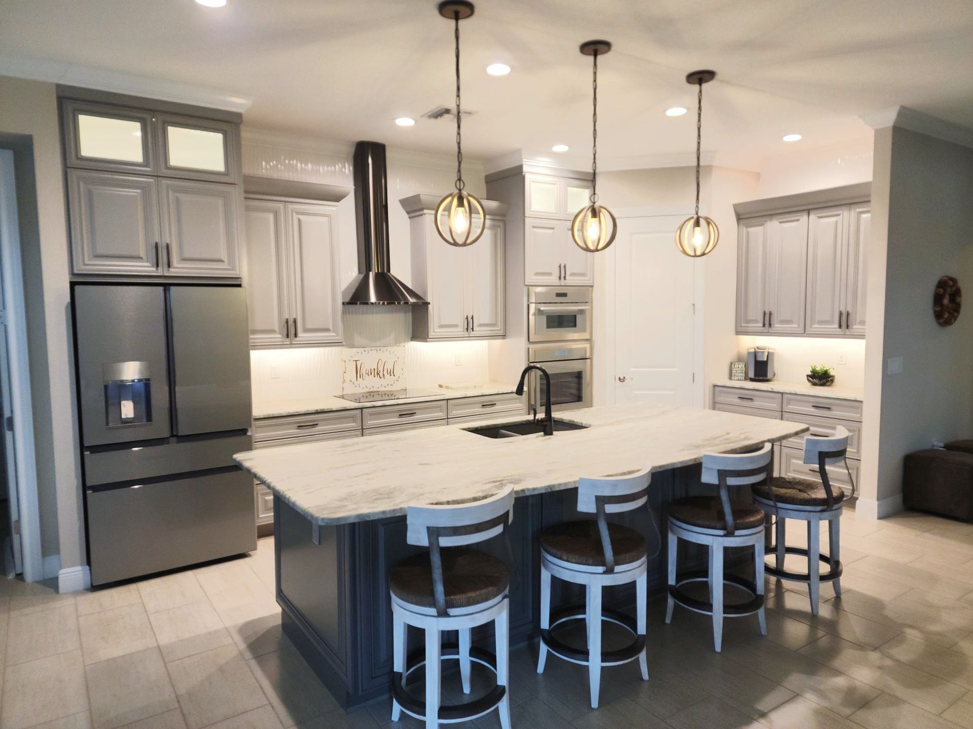 Modern kitchen with gray cabinets, stainless steel appliances, and a marble island with bar stools.