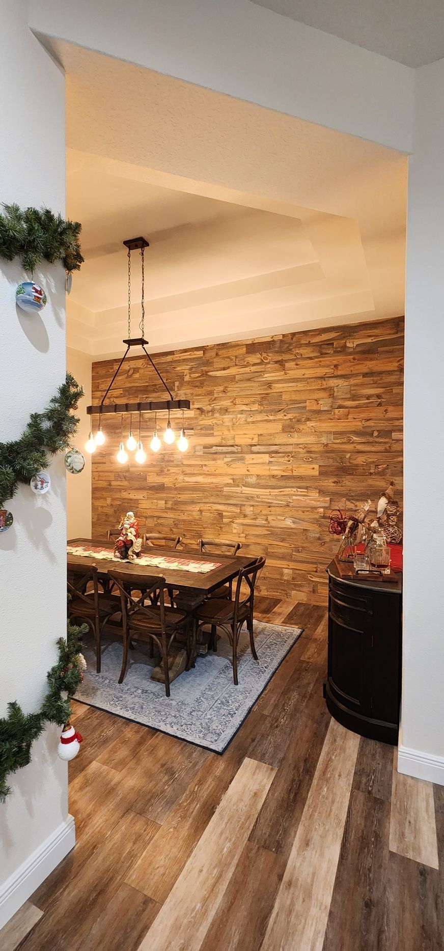 Dining room with wood plank accent wall, dark wood table, chairs, and light fixture.