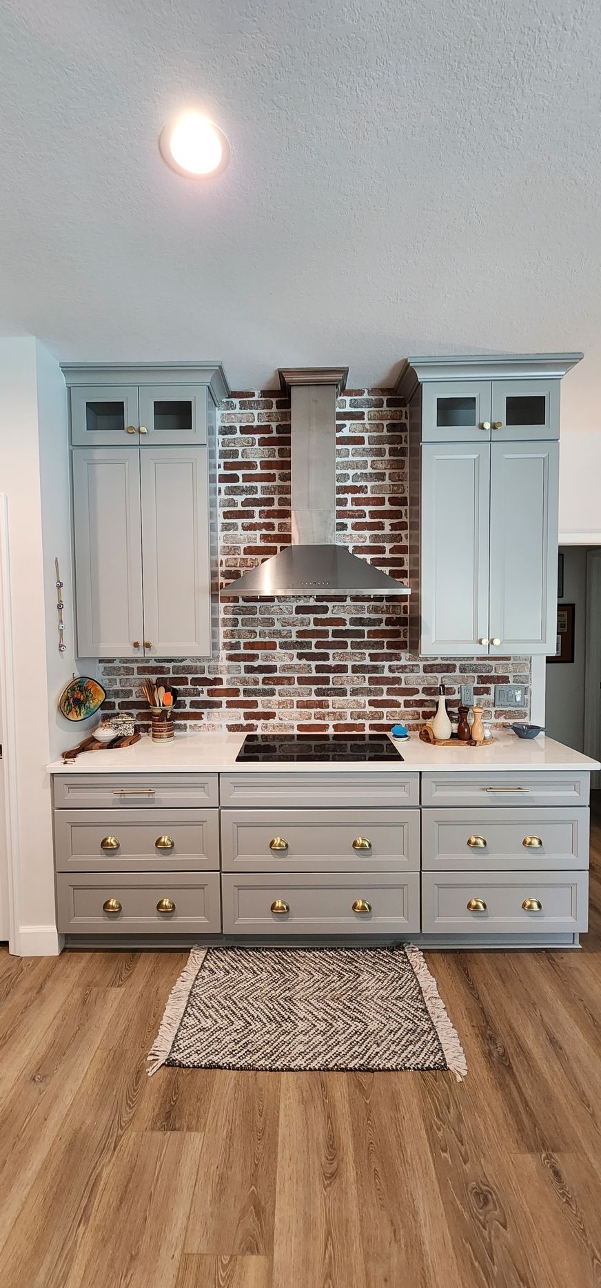 Kitchen with gray cabinets, brick backsplash, stainless steel hood, and wooden floor.