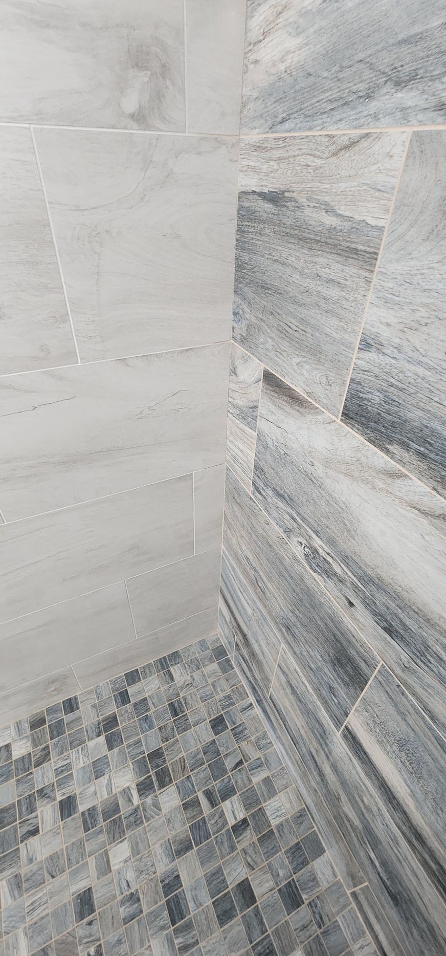 Shower with textured gray and blue tiles, mosaic floor.