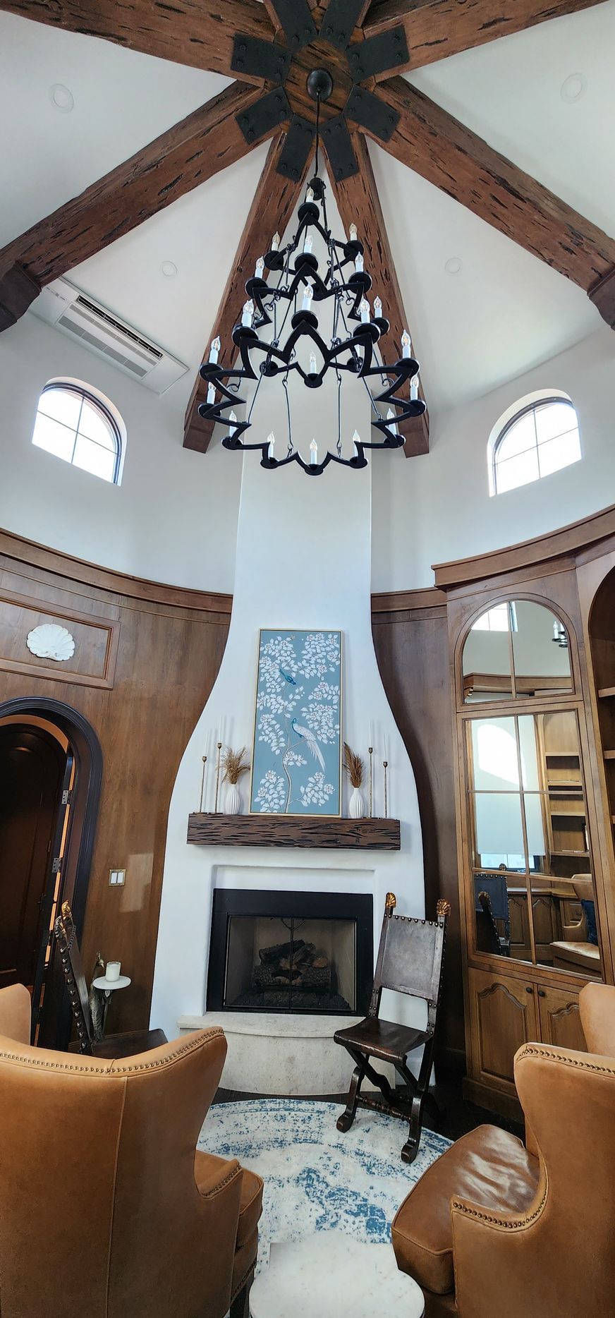 Elegant living room with fireplace, chandelier, wood beams, and leather chairs.