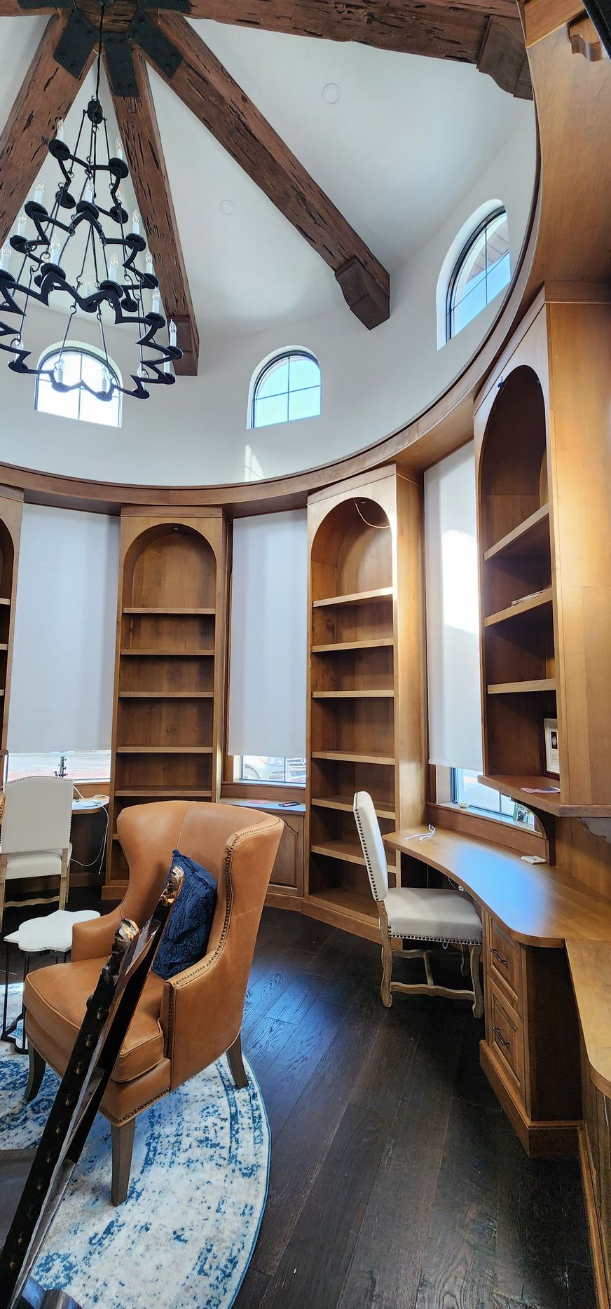 A circular library with wooden bookshelves, desks, and seating, under a domed ceiling with a chandelier.
