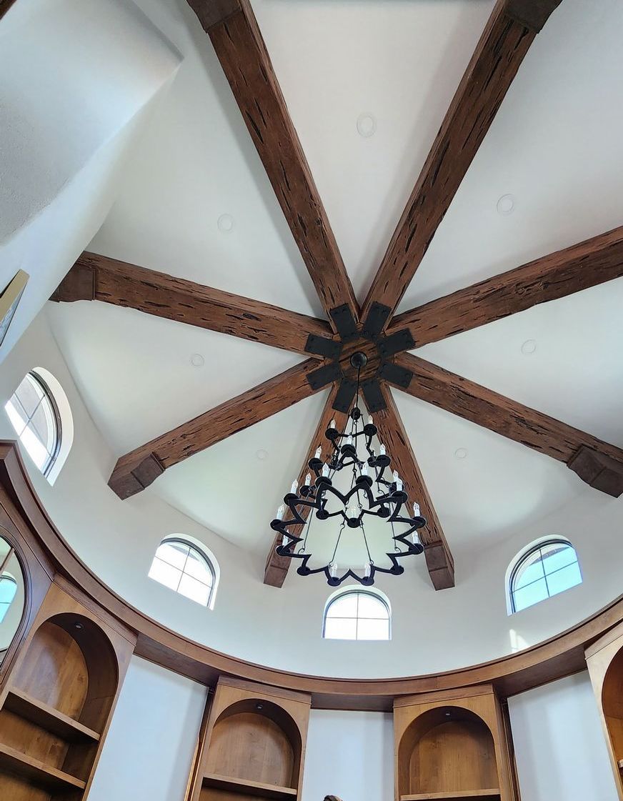 Circular room with wooden beams radiating from center, chandelier, arched windows, and built-in bookshelves.