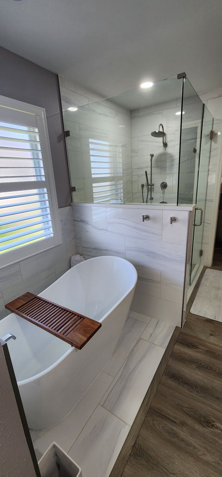 Modern bathroom with a freestanding tub, glass shower, and wooden flooring.