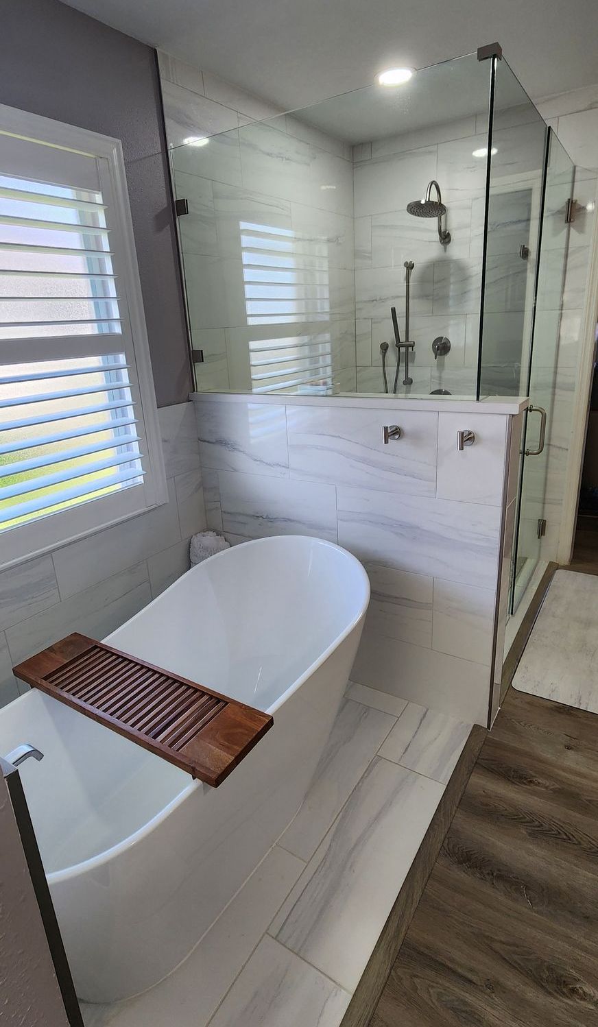 Modern bathroom with a white tub, glass shower, and light tile.
