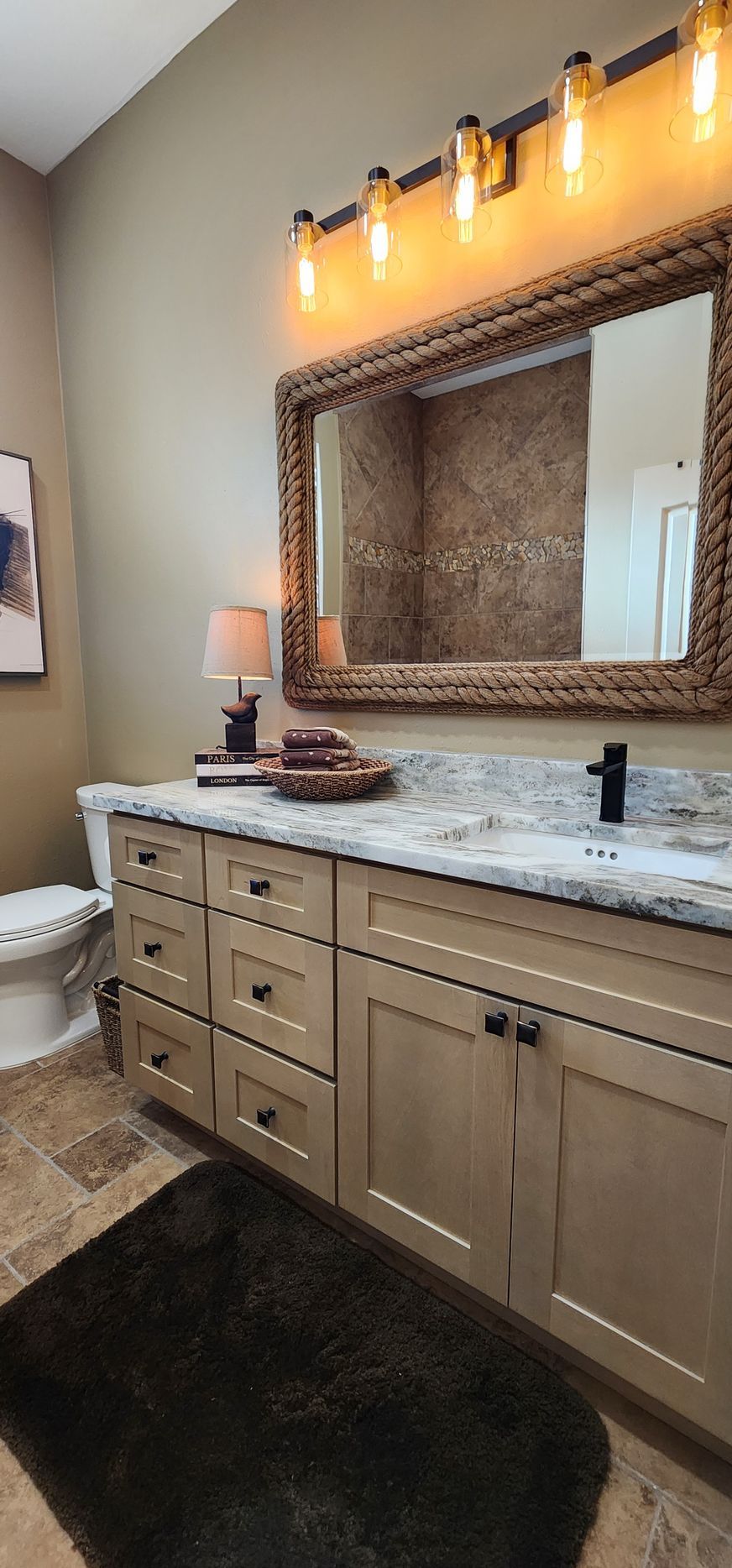 Bathroom vanity with mirror, light fixtures, and rug; neutral colors.