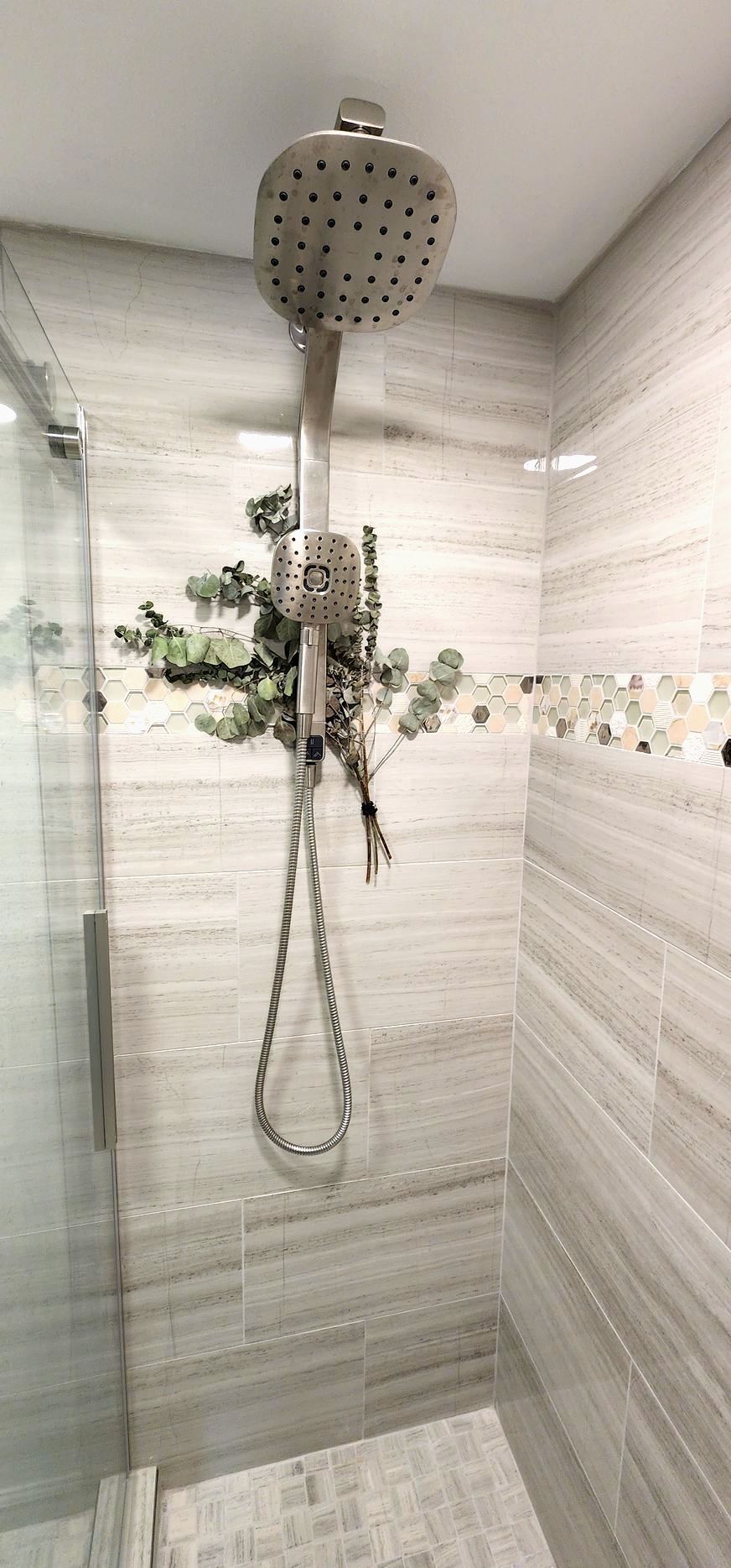 Shower with light gray tile walls and a silver showerhead. Greenery hangs from the showerhead.