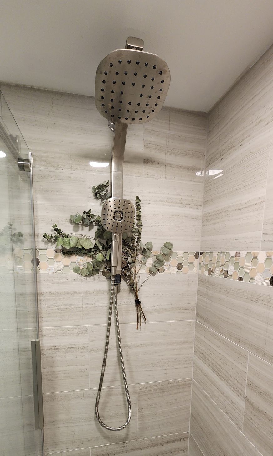 Showerhead in a tiled shower. Eucalyptus hanging from the shower arm.