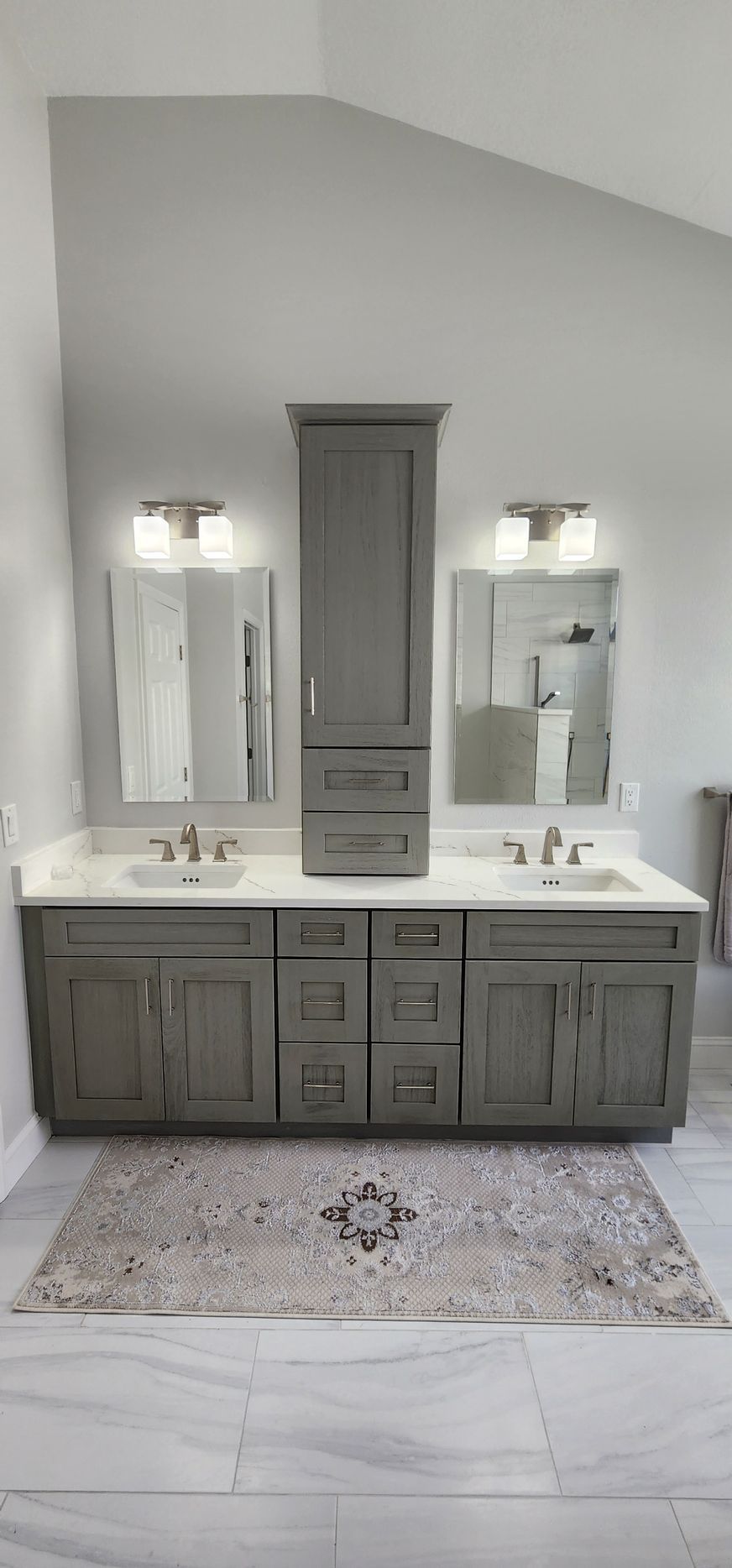 Gray bathroom vanity with mirrors, lights, and a rug.
