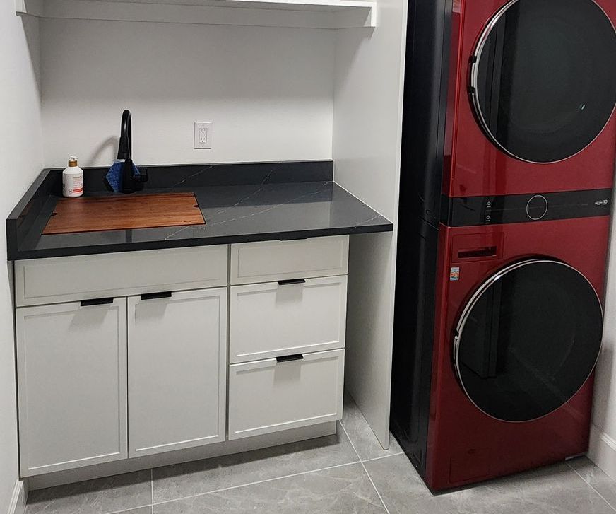 Laundry room with a red stacked washer/dryer, white cabinets, and a sink with a black faucet.