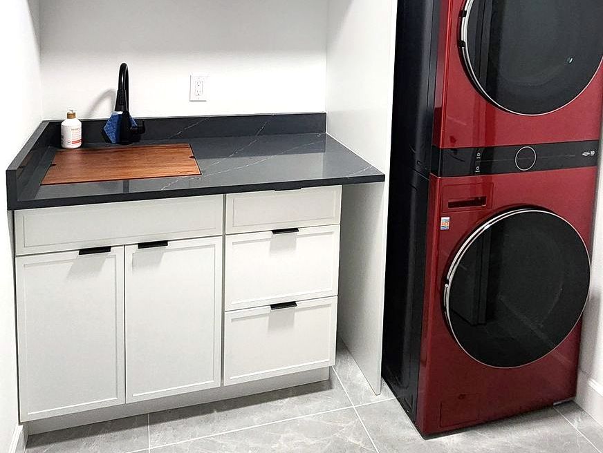 Laundry room: white cabinets, gray countertop with sink, stacked red washer/dryer.