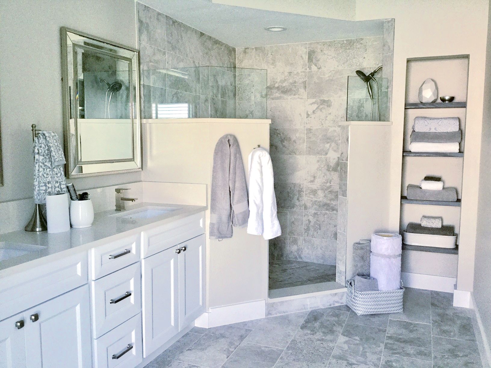 Bathroom with white vanity, gray tile shower, built-in shelves with towels.