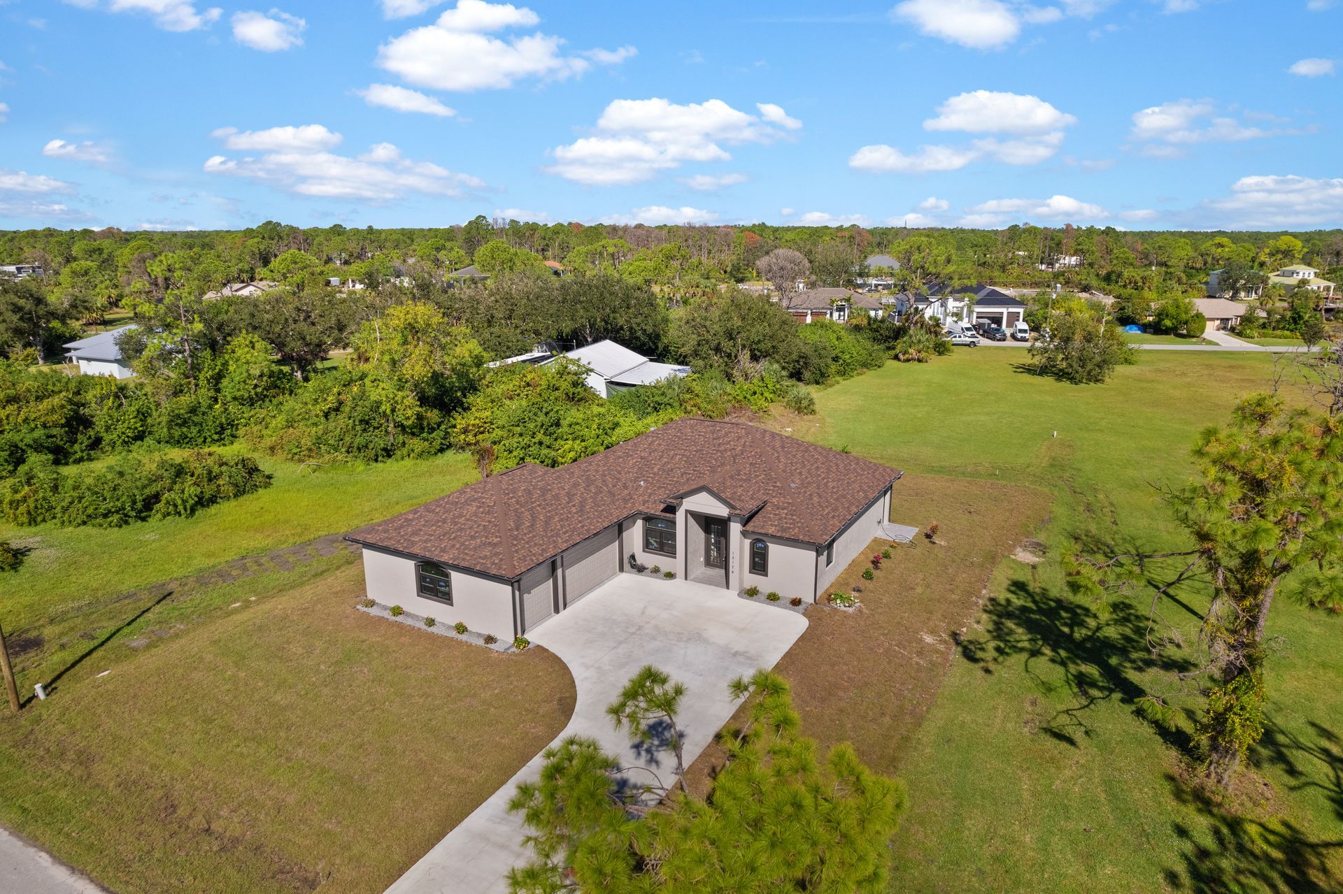 Aerial view of a modern one-story house with a brown roof, gray exterior, and a large green yard.
