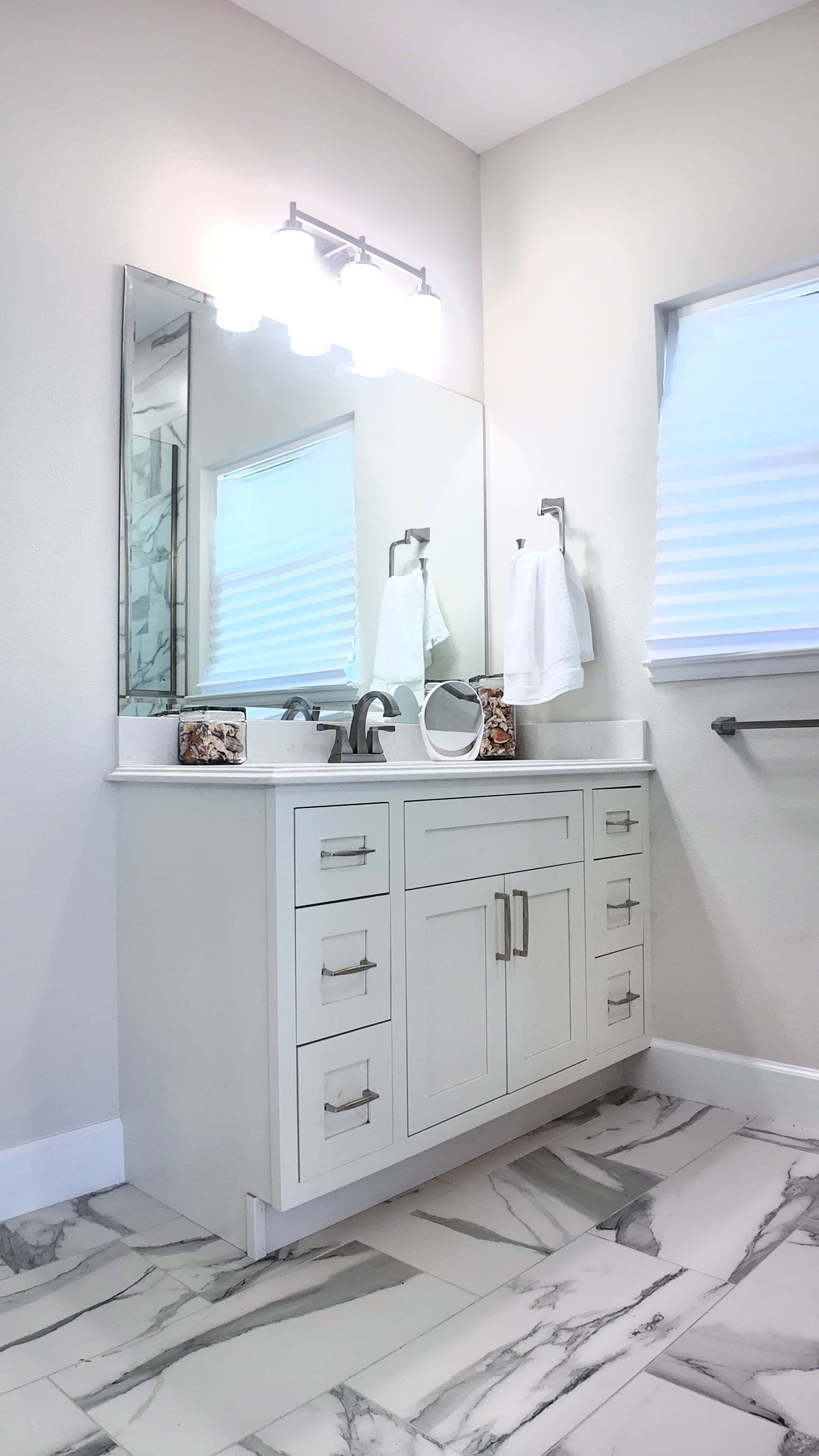 White bathroom vanity with a mirror, white countertop, and marble-look floor.