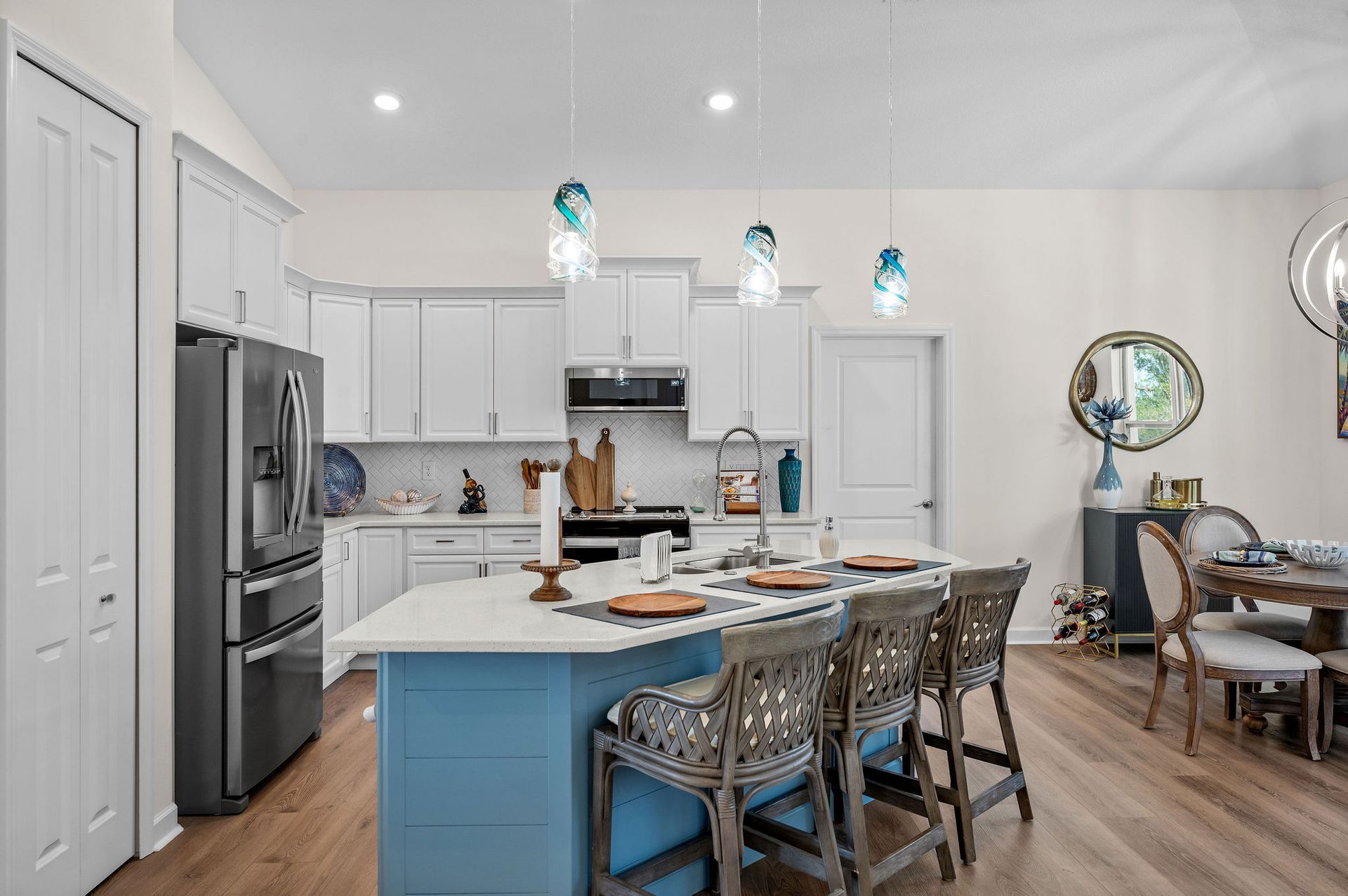 A modern kitchen with blue island, white cabinets, hardwood floors, and dining area.