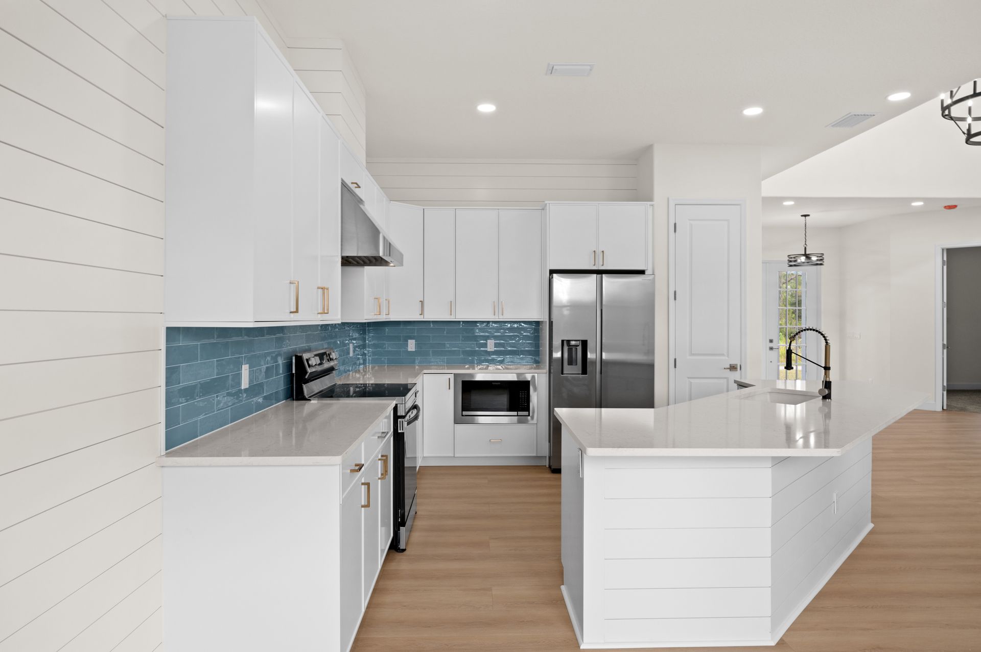 Modern white kitchen with stainless steel appliances, blue tile backsplash, and an island.