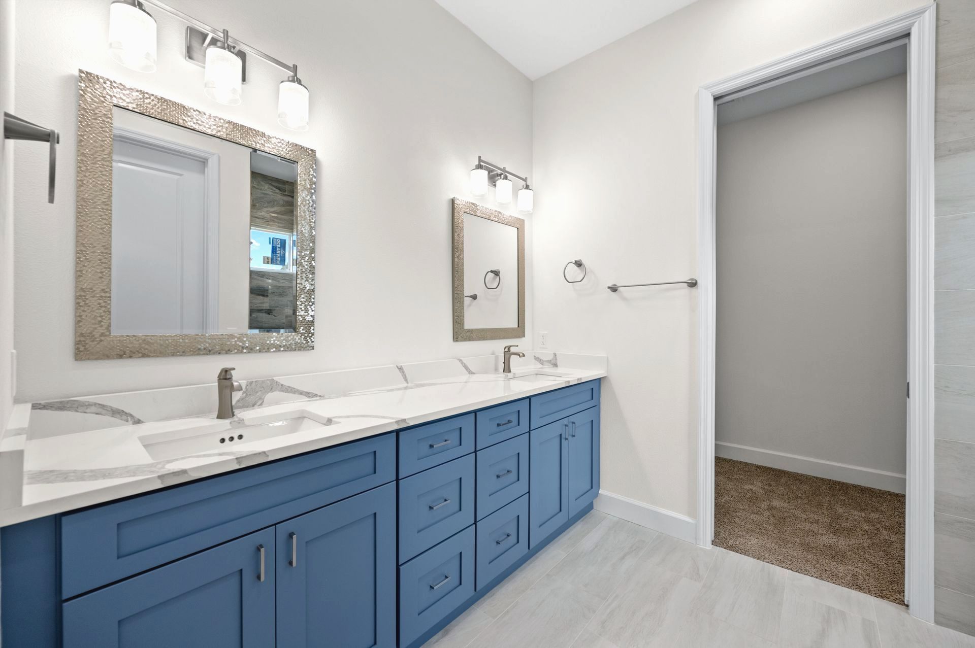 Blue vanity with marble counters and silver fixtures in a modern bathroom.