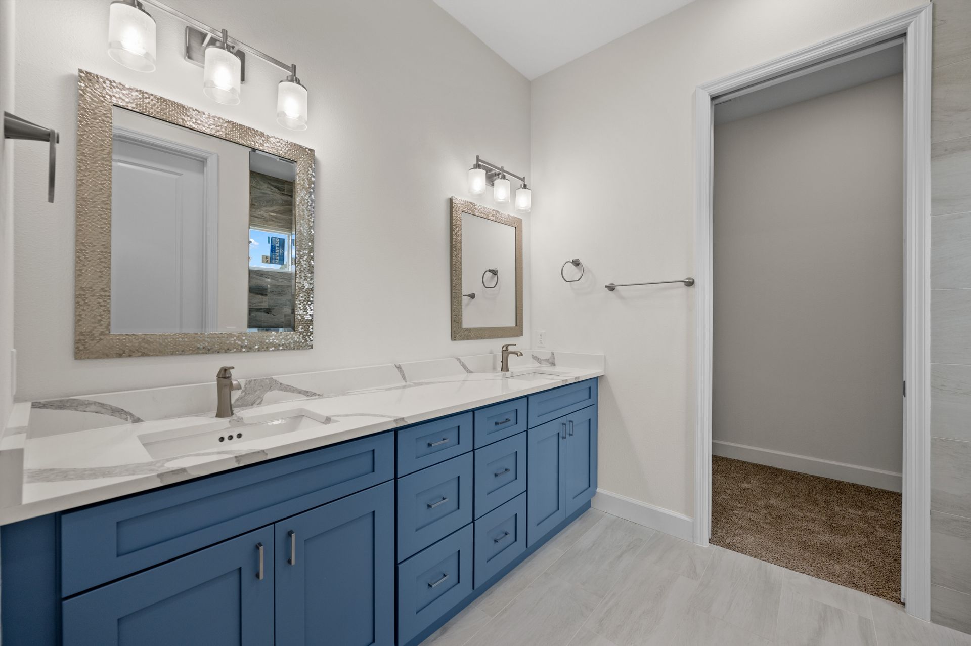 Blue vanity with two sinks, mirrors, and lights in a modern white bathroom.