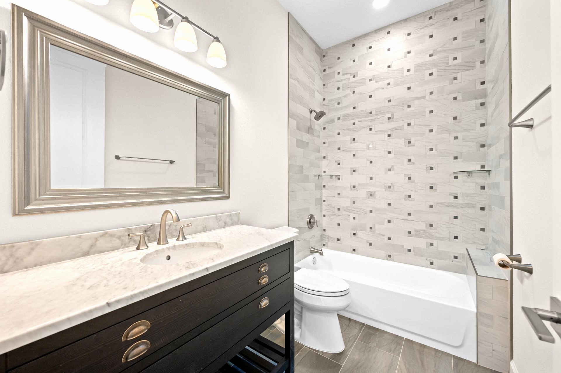 Bathroom with dark vanity, large mirror, bathtub, and patterned tile wall.