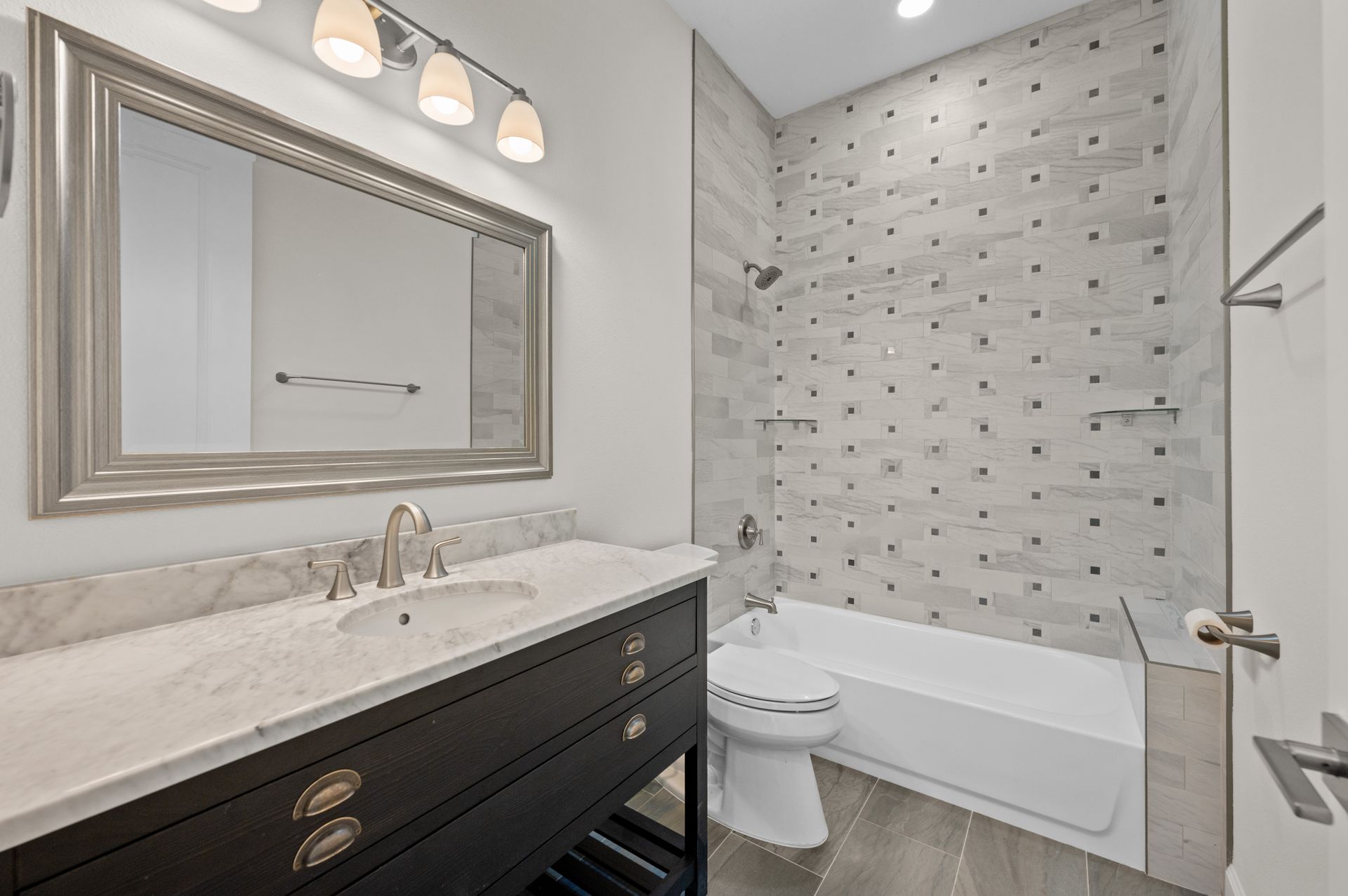 Bathroom with dark vanity, large mirror, tub, and patterned shower tiles.