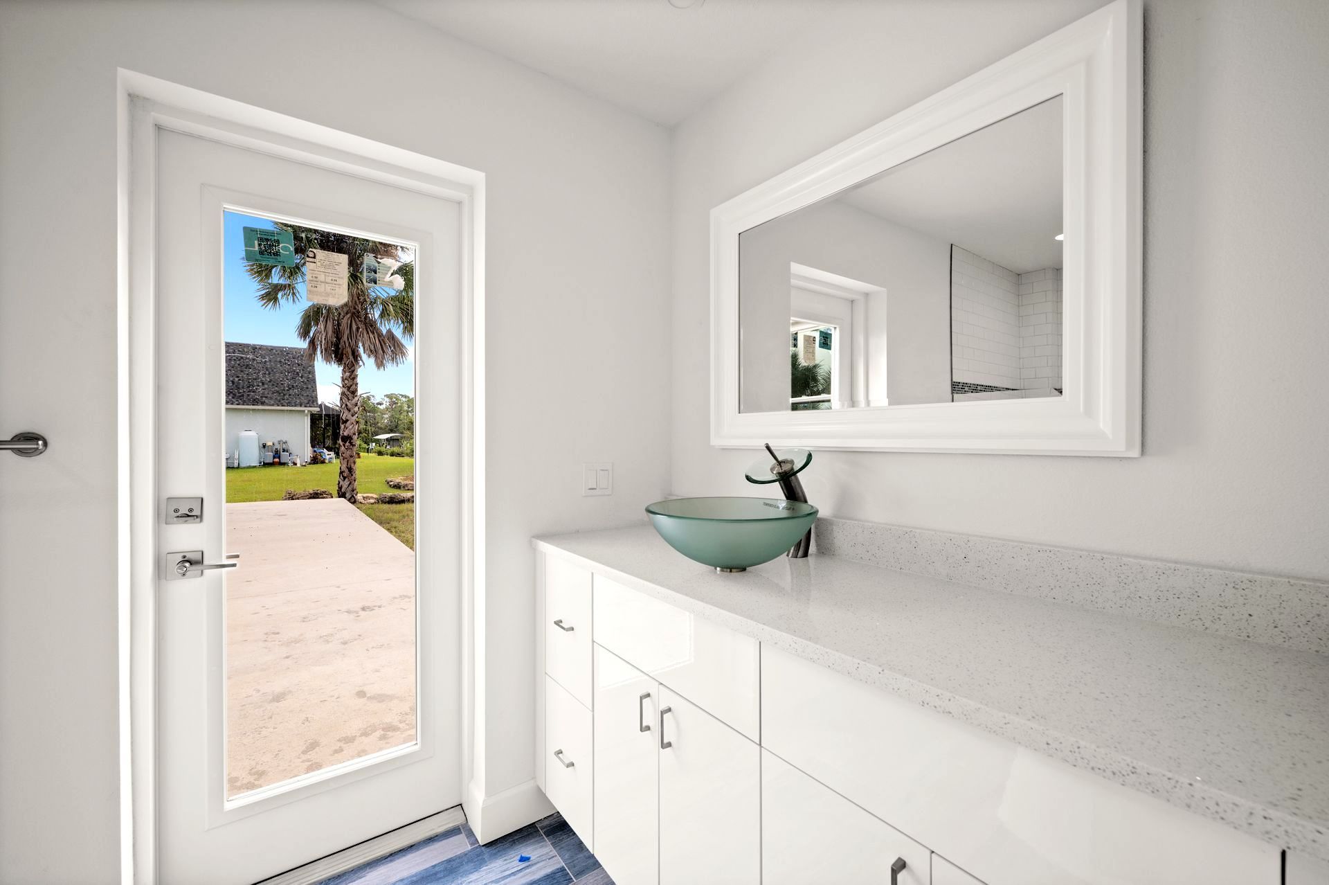 Bathroom with a white vanity, glass bowl sink, large mirror, and a door overlooking a yard.