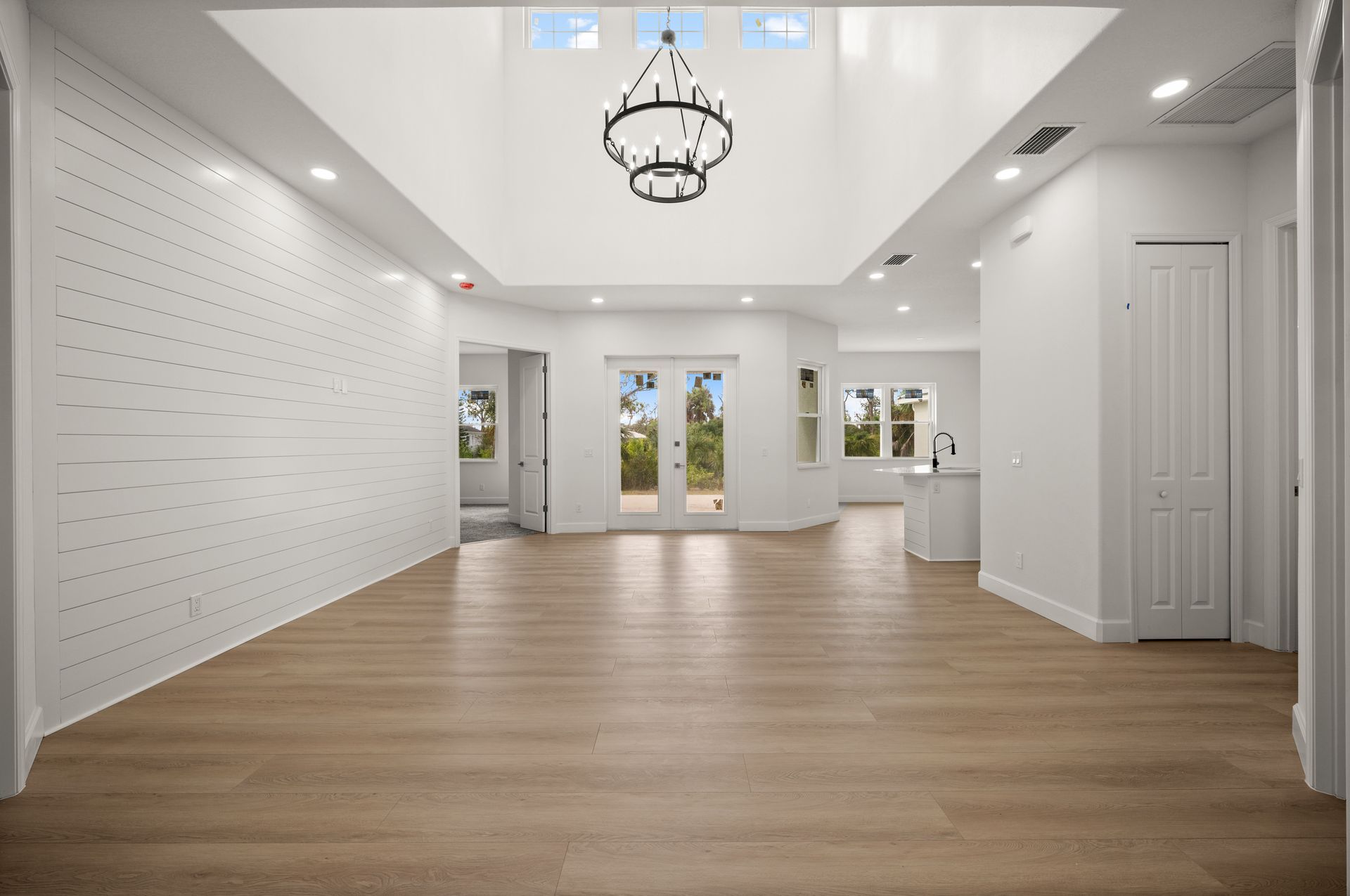 Spacious, modern interior with light wood floors, white walls, chandelier, and skylight.