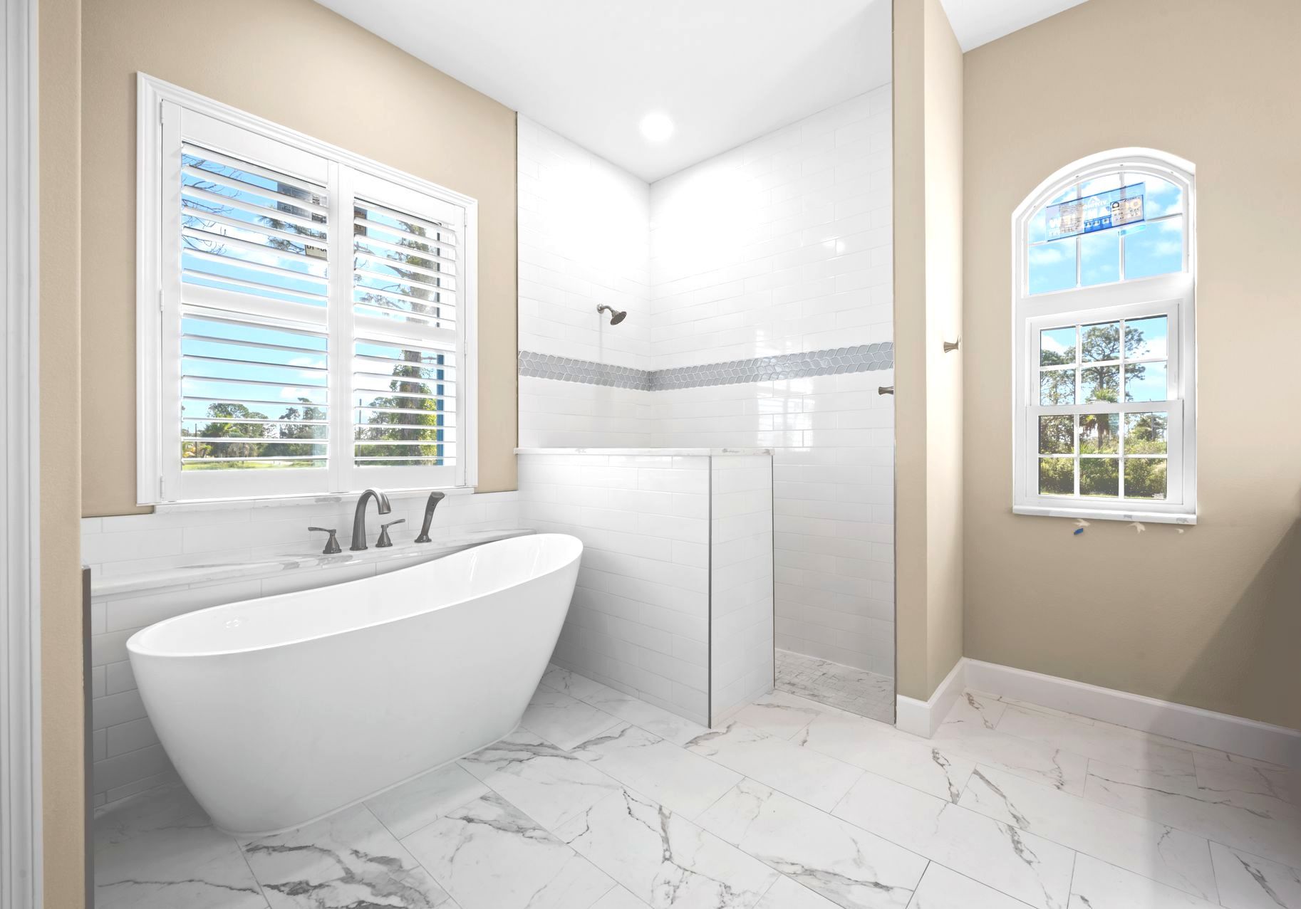 A modern bathroom with a white soaking tub, marble tile, and a walk-in shower.