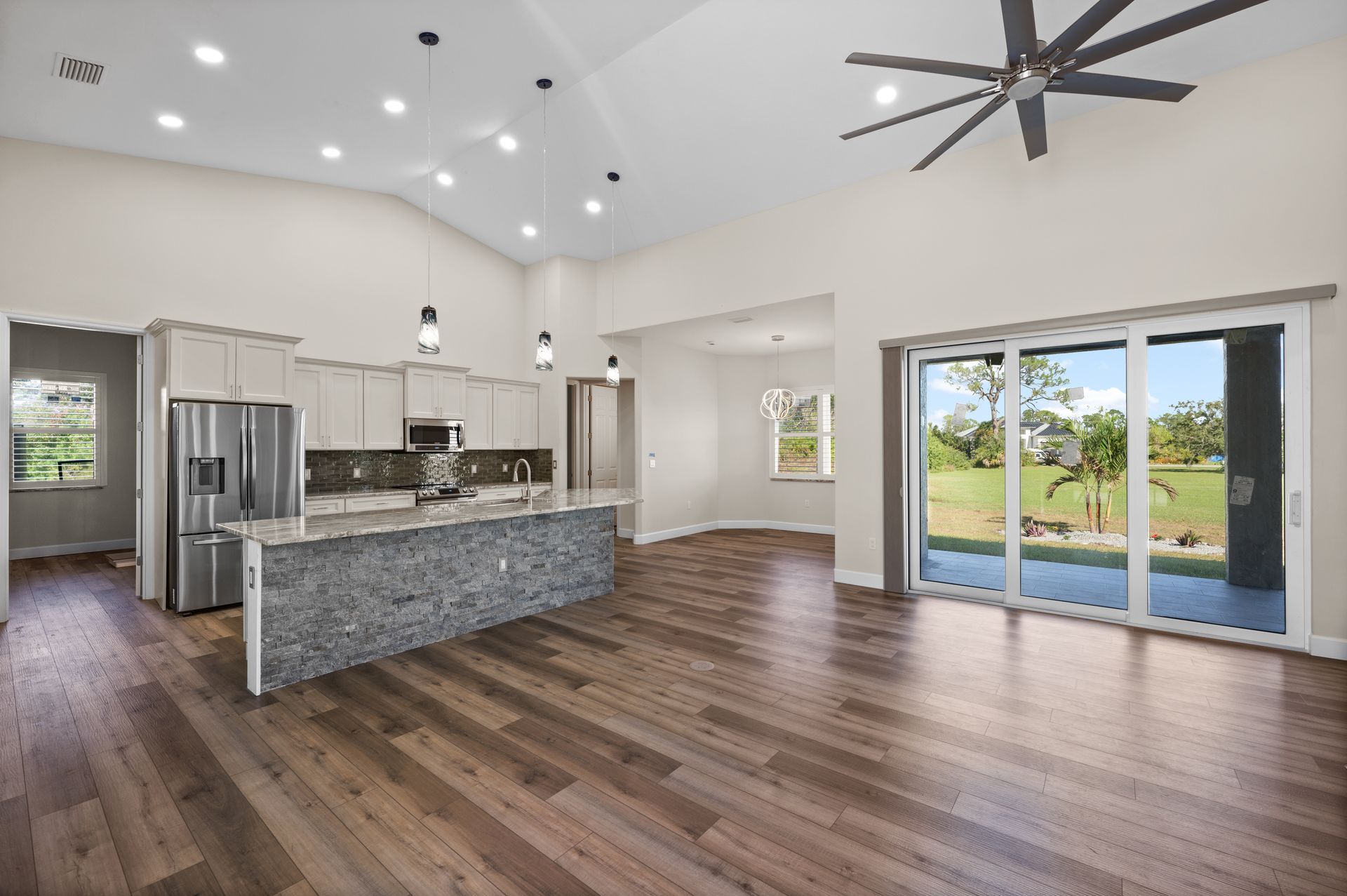 Open-concept kitchen and living area with gray island, wooden floors, and large sliding glass doors.