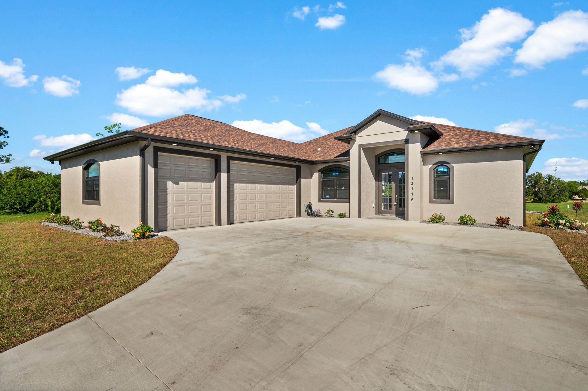 Tan stucco house with a tile roof, three-car garage, and a concrete driveway under a blue sky.