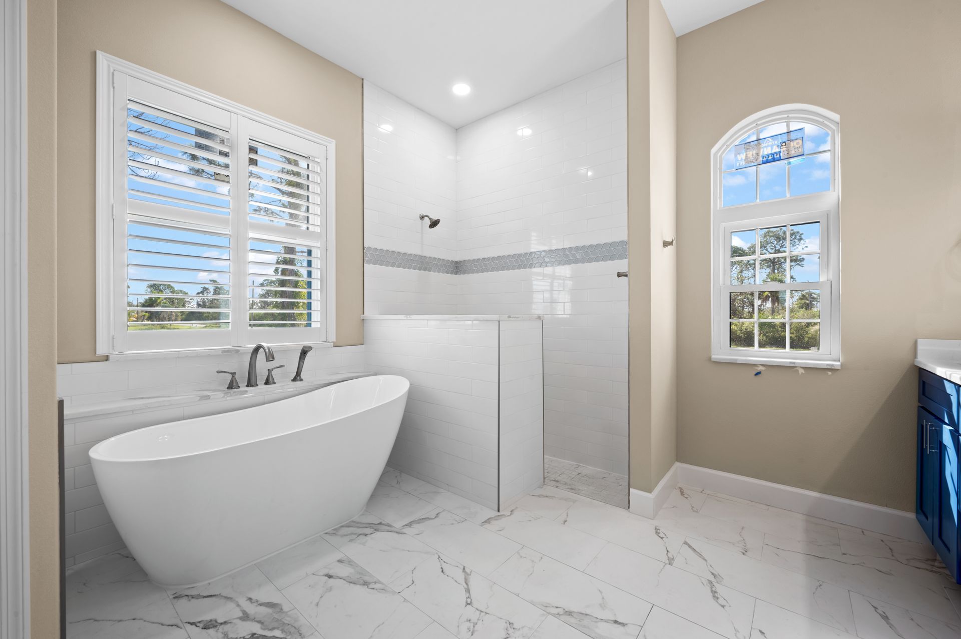 Modern bathroom with a free-standing tub, large shower, marble floors, and a shuttered window.