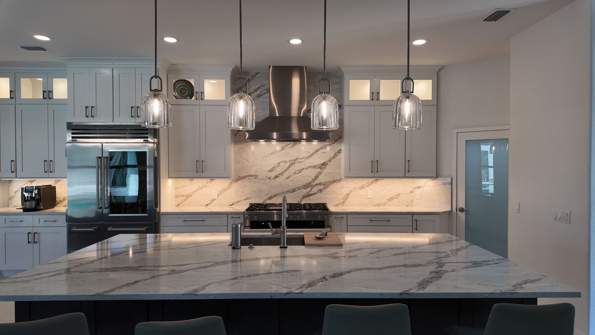 Modern kitchen with marble countertops, stainless steel appliances, and pendant lights.