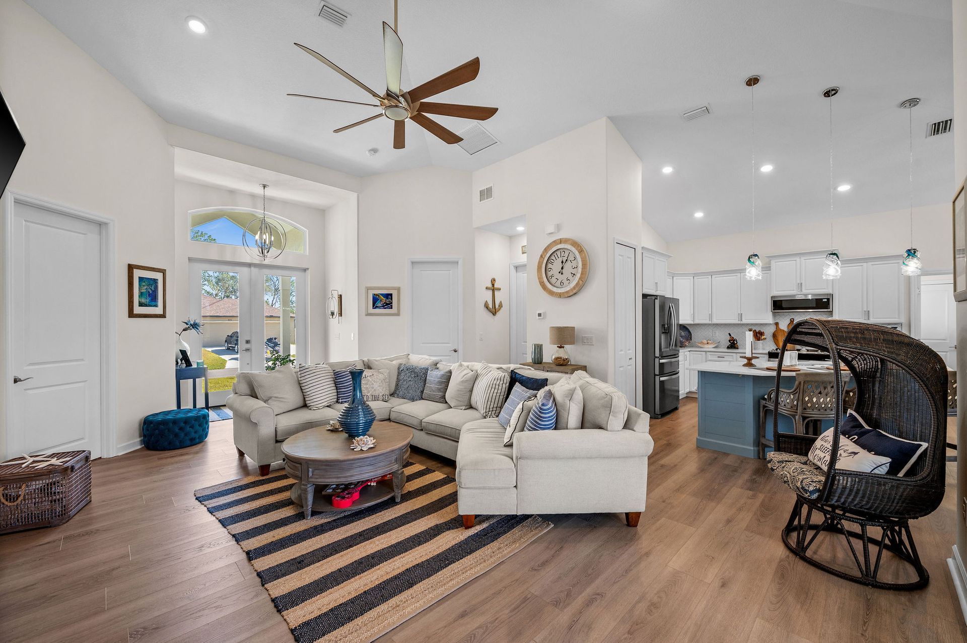 Spacious, coastal-style living room with sectional sofa, striped rug, and open kitchen in the background.