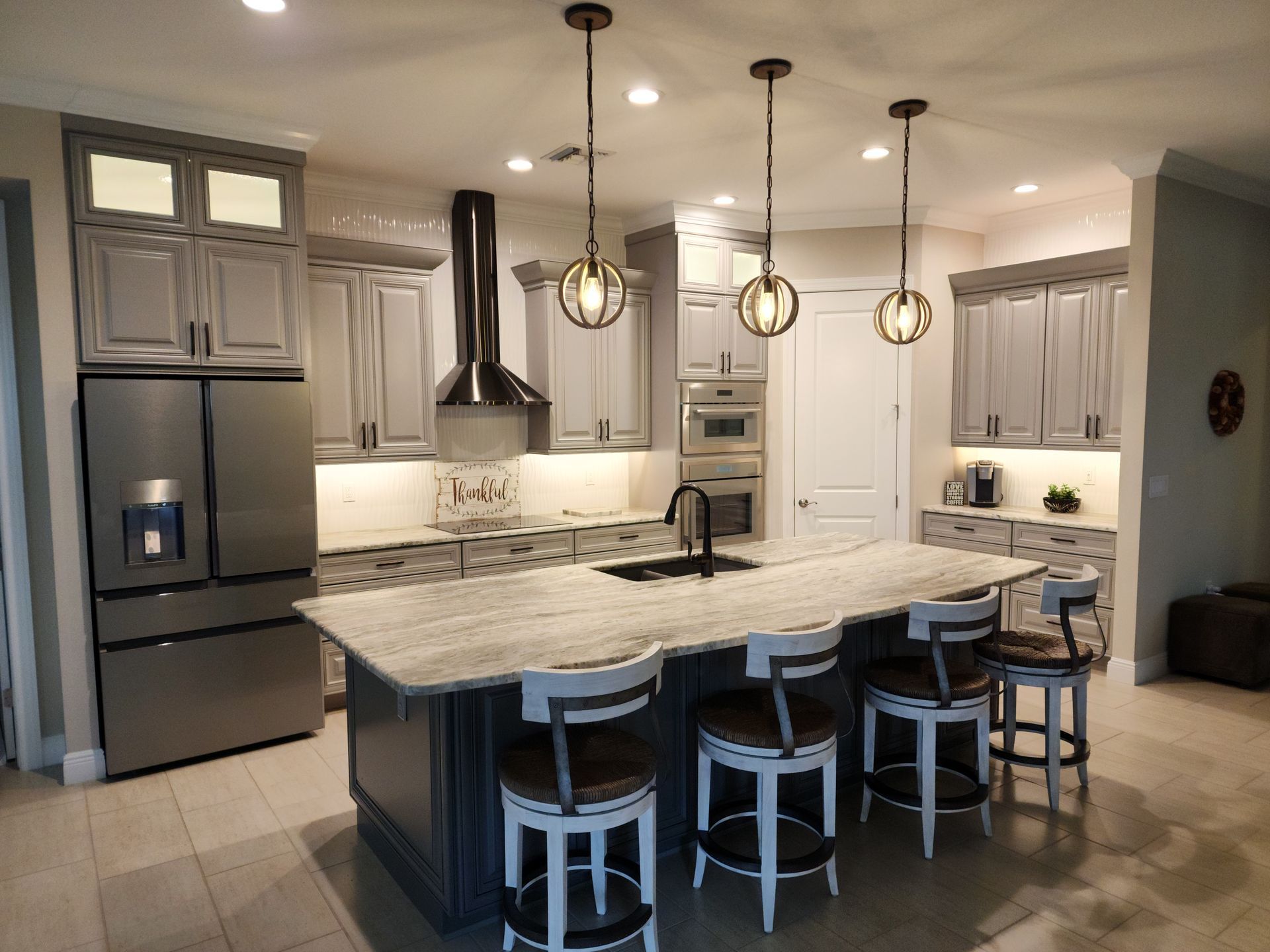 Gray kitchen with island, pendant lights, stainless steel appliances, and bar stools.