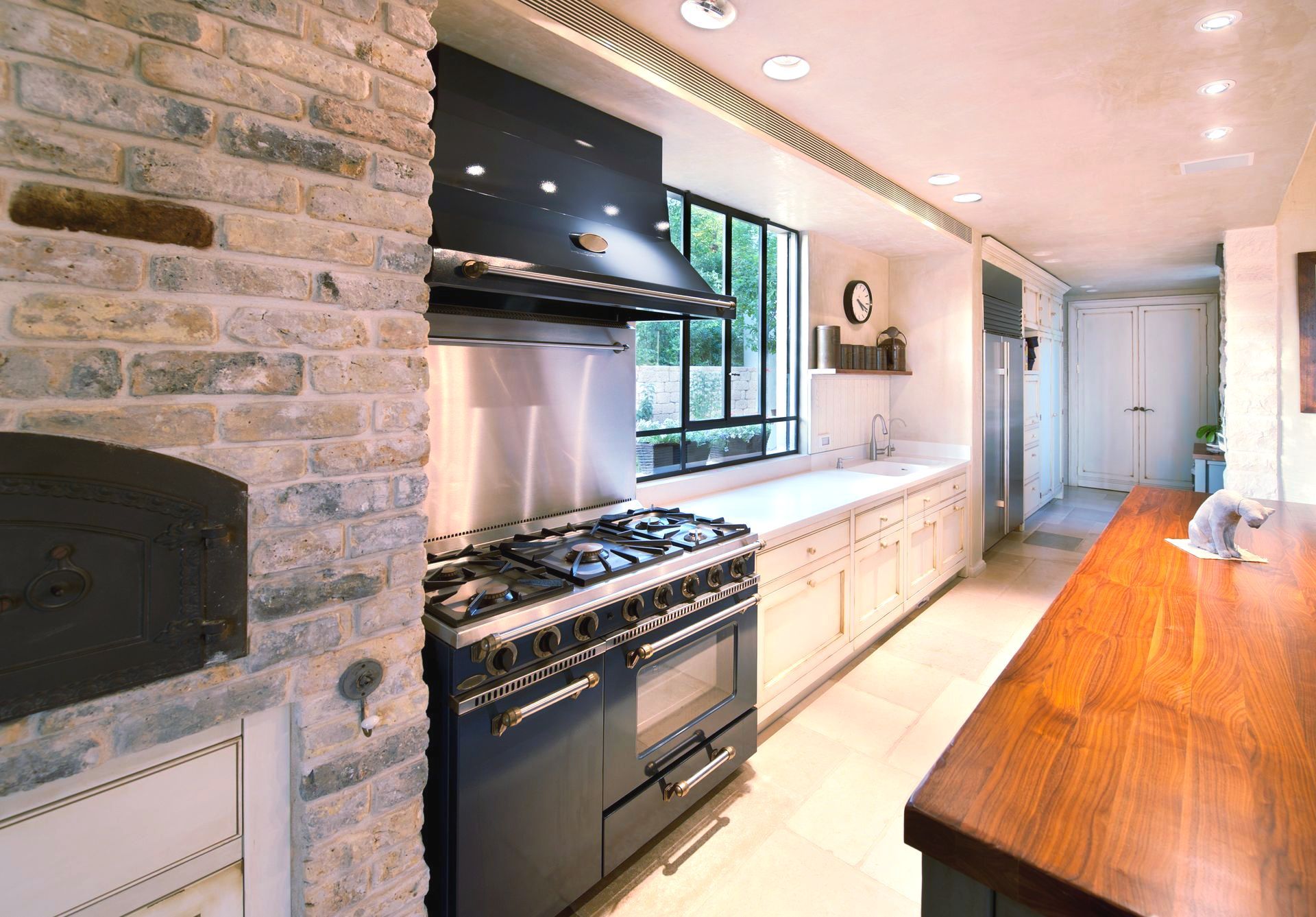 A modern kitchen with brick walls, a black stove, and a wooden countertop.