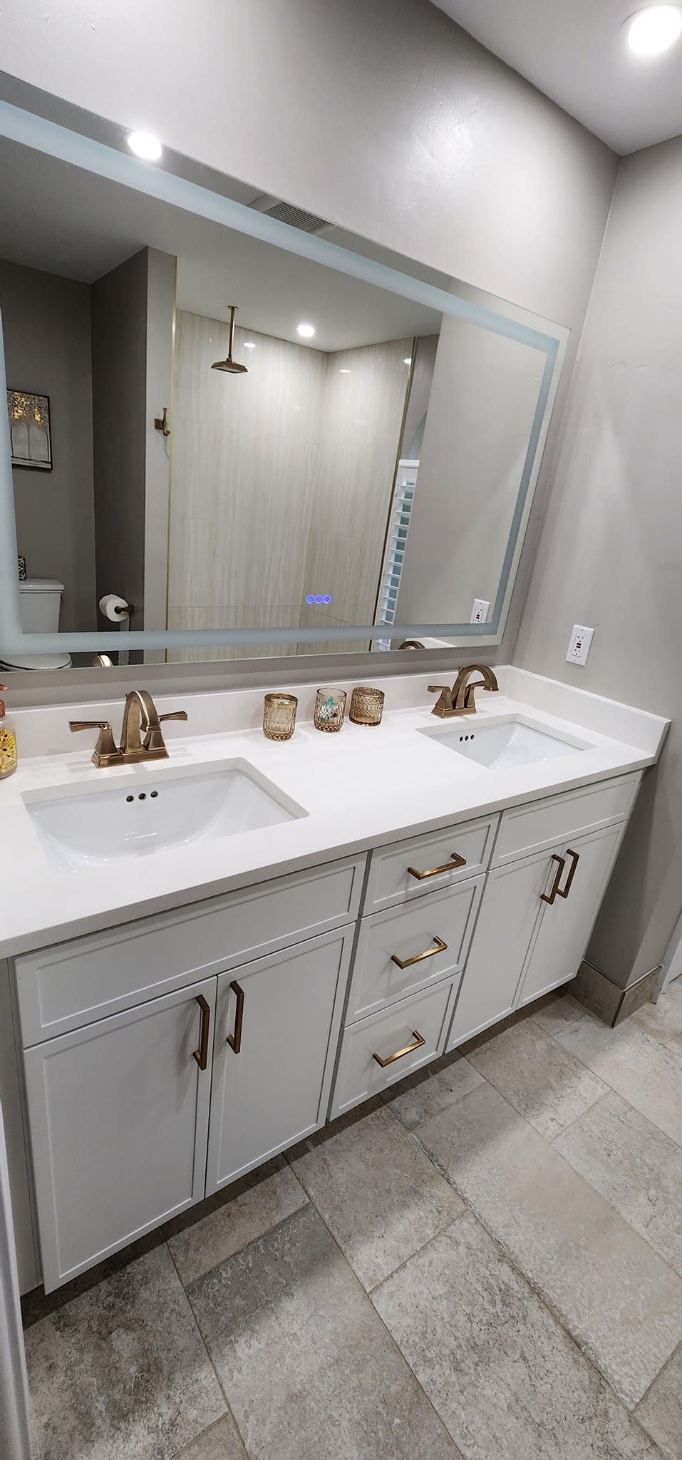 Modern bathroom with a white double sink vanity, gold faucets, and a large mirror.