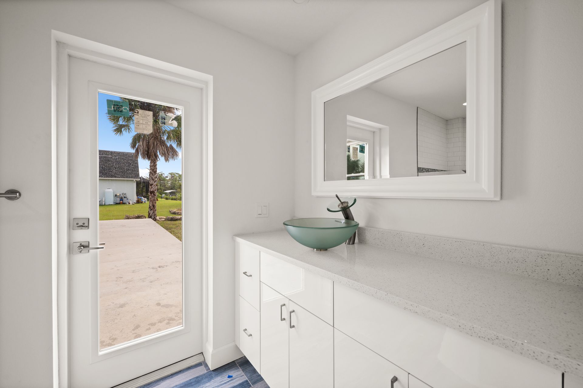 Bathroom with white vanity, glass bowl sink, and a door opening to a sunny yard.