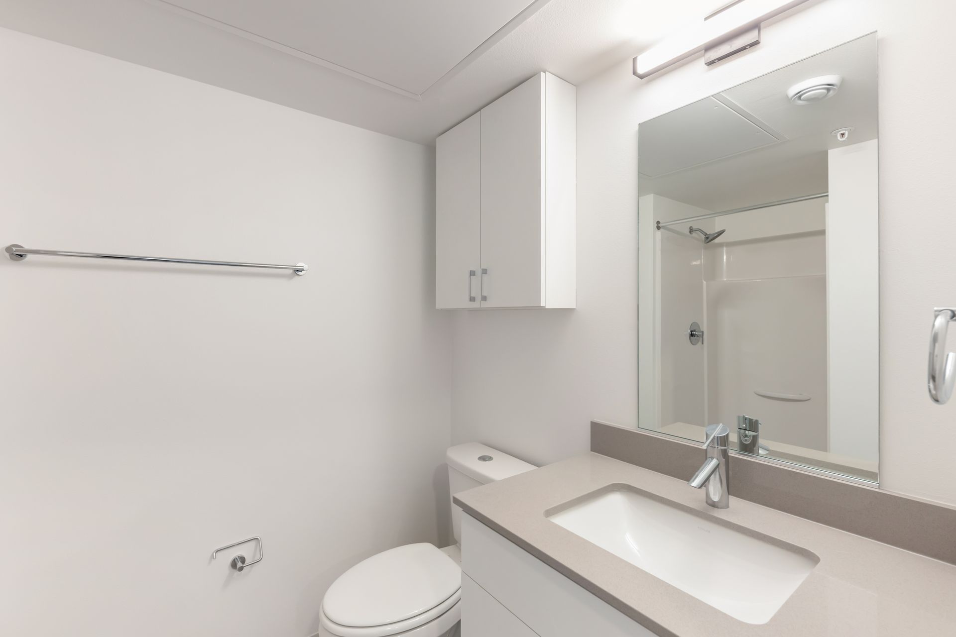 Small, white bathroom with a toilet, sink, mirror, and shower.