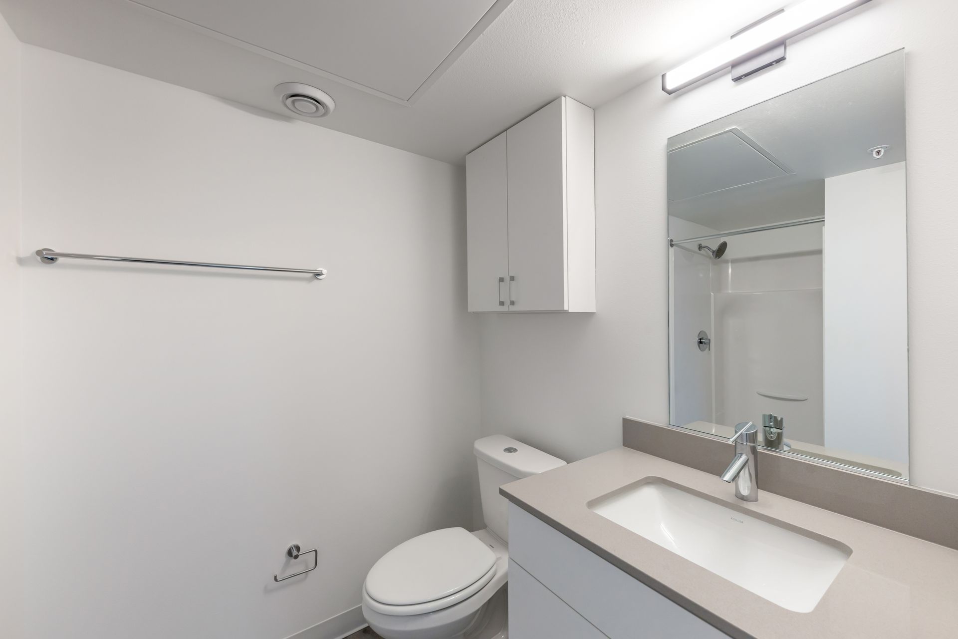 Bathroom with white walls, toilet, vanity, and a mirror.