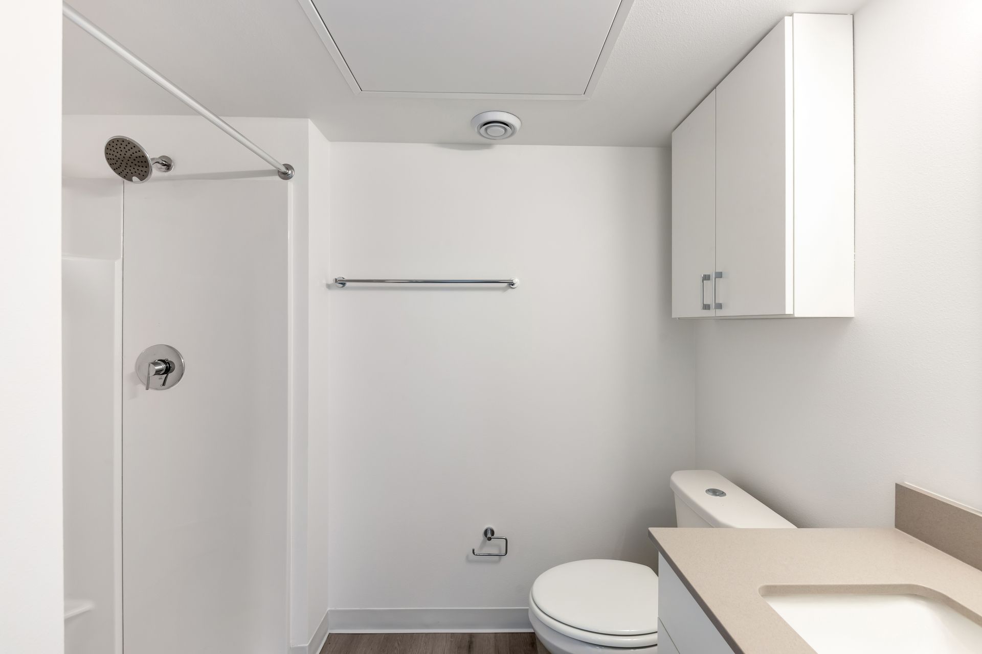 Bathroom with white walls, shower, toilet, cabinet, and towel rack.