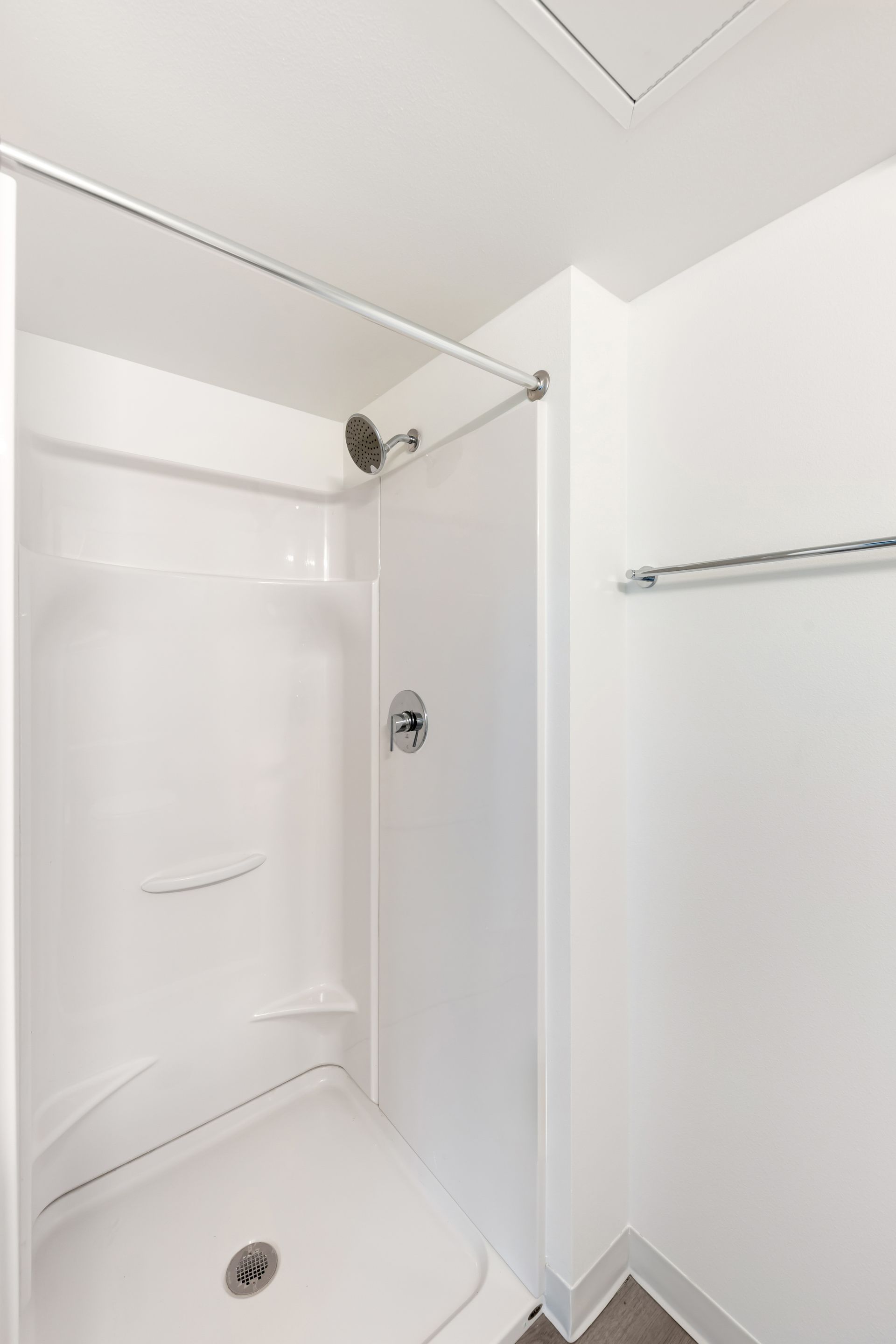 White, walk-in shower with a chrome showerhead and bar, with a towel rack on a white wall.
