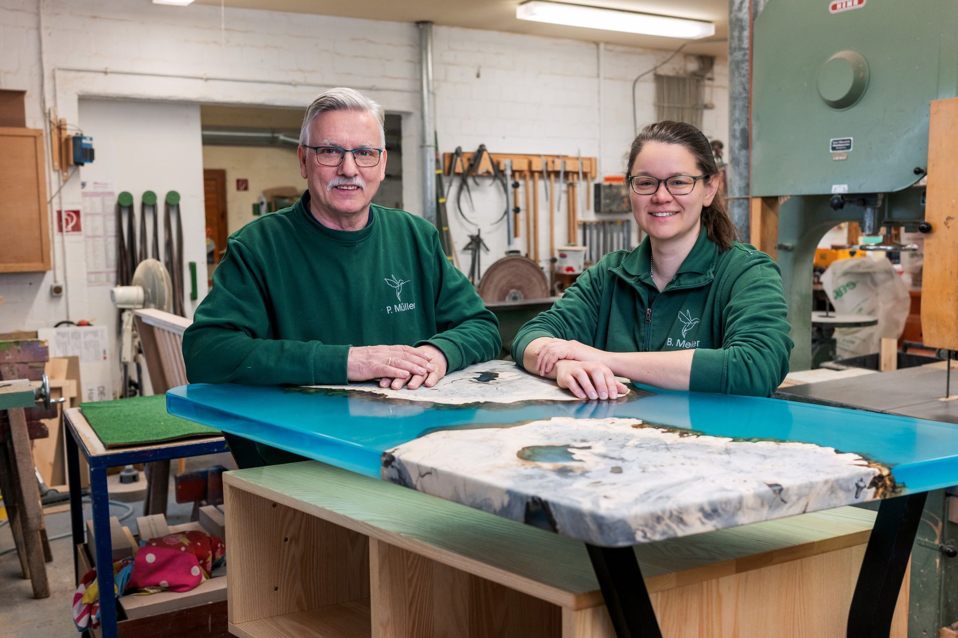 Ein Mann und eine Frau sitzen in einer Werkstatt an einem Tisch.