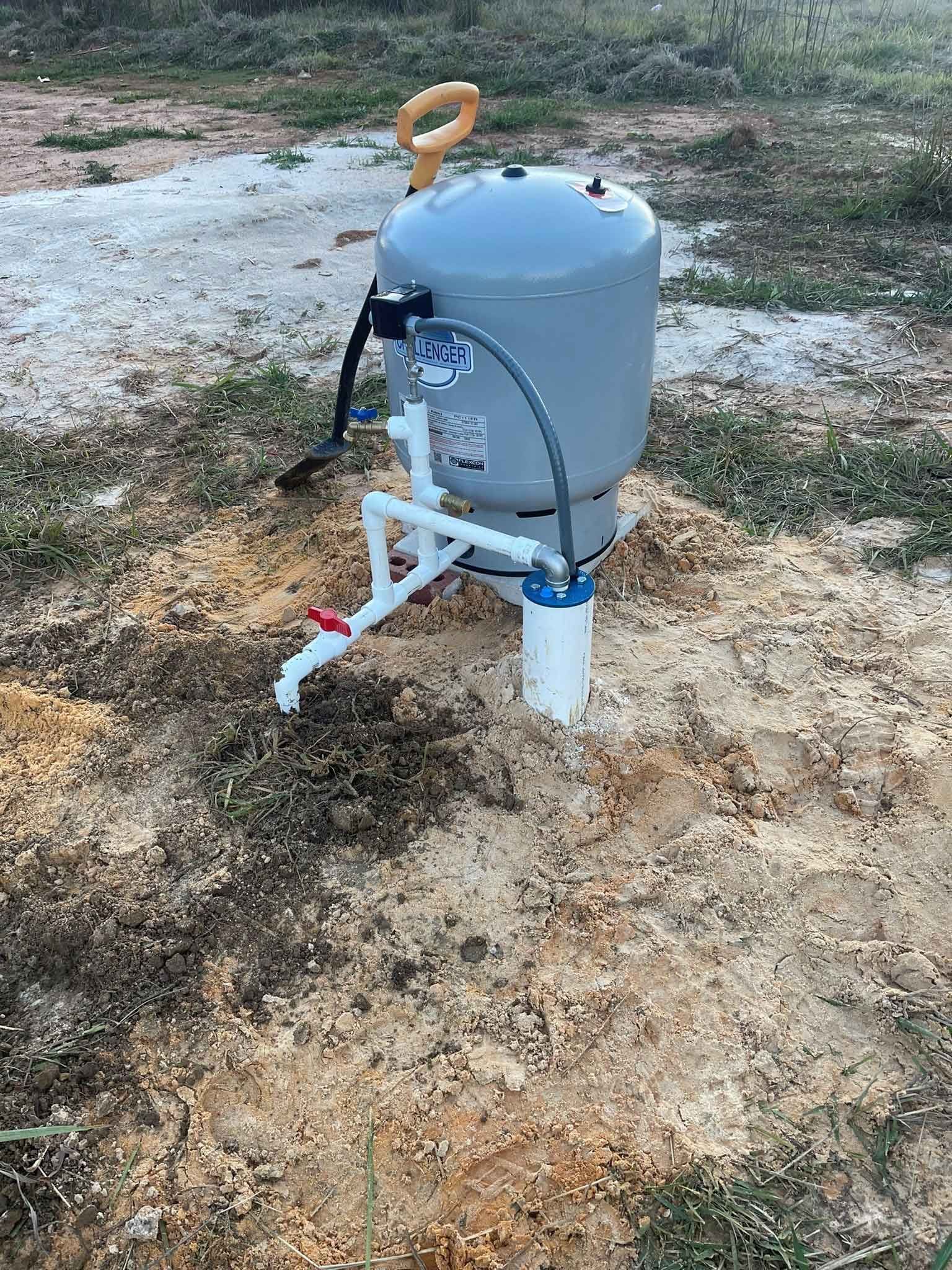 A water tank is sitting in the middle of a dirt field.