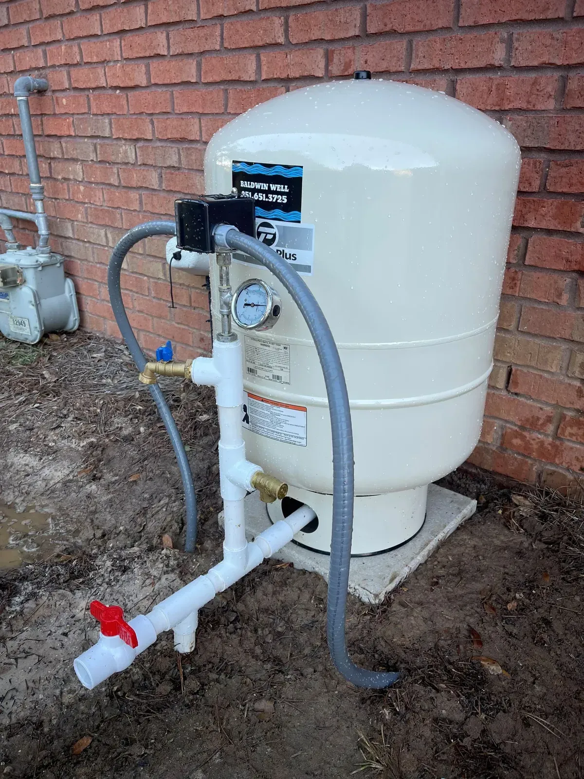 A white water tank is sitting next to a brick wall.
