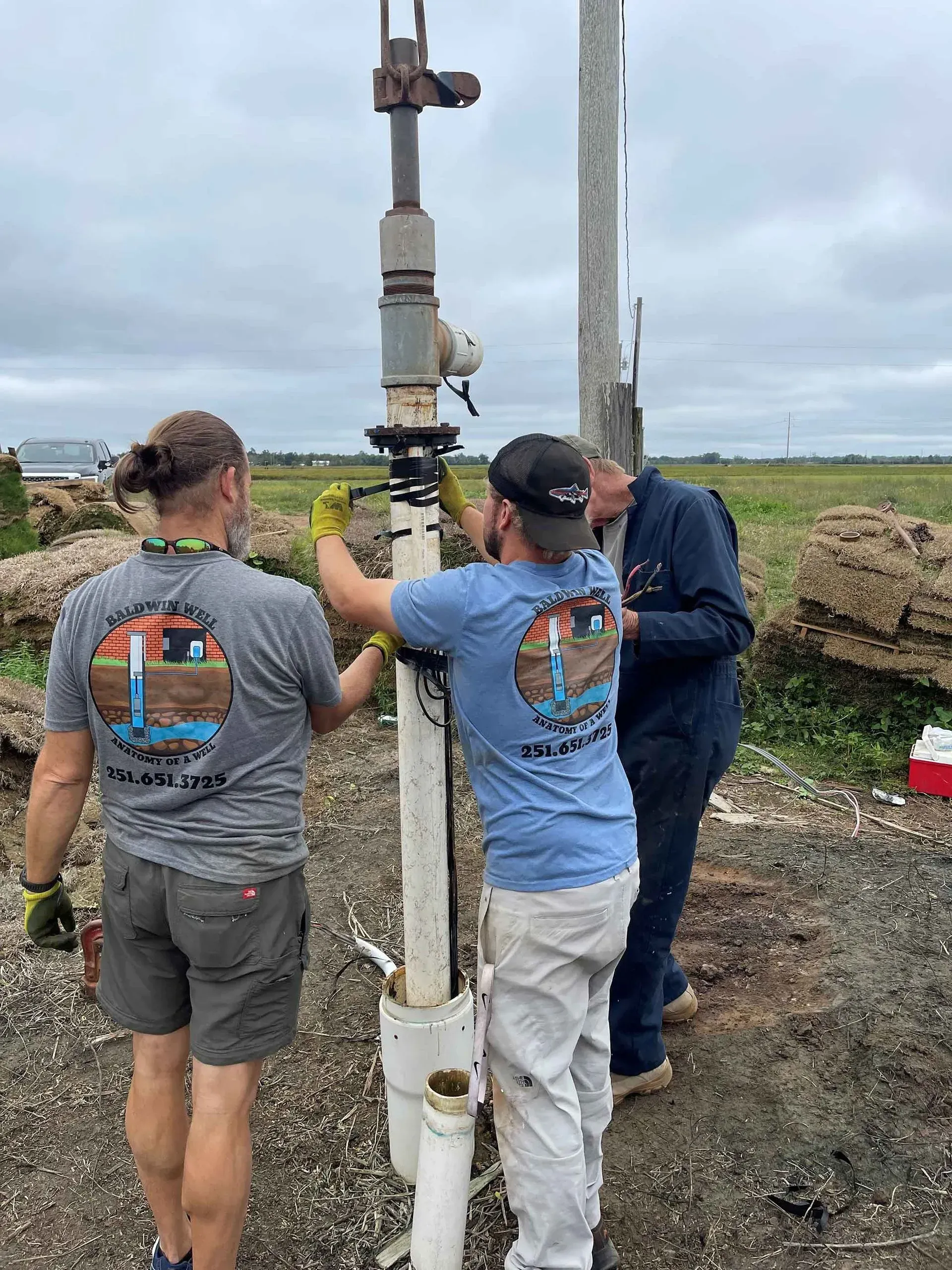 Two men are working on a pipe in a field.