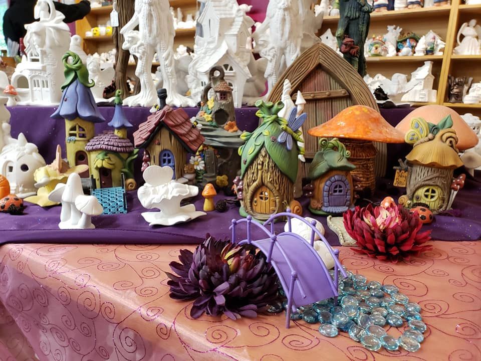 A display of ceramic fairy houses and decorations on a purple tablecloth.