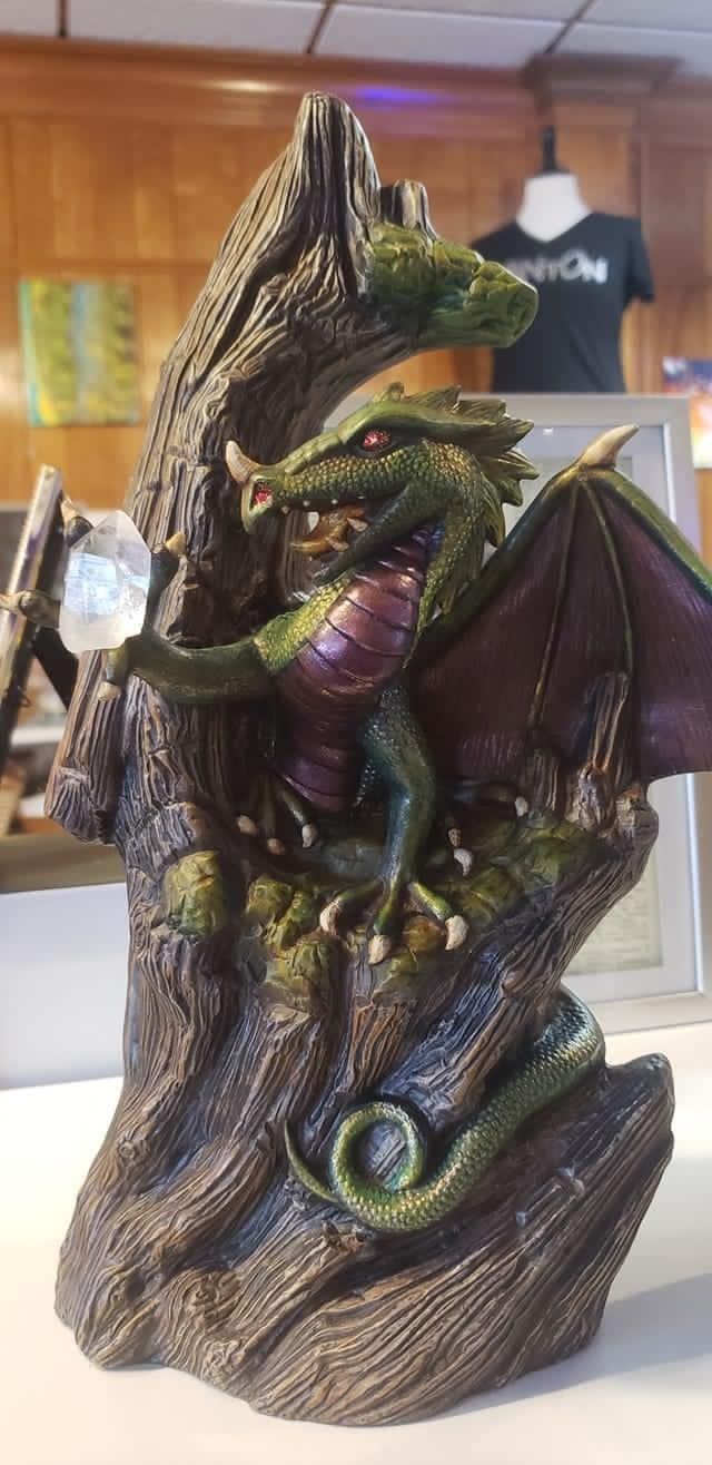 A green and purple dragon statue perched on a brown tree trunk, holding a clear orb.